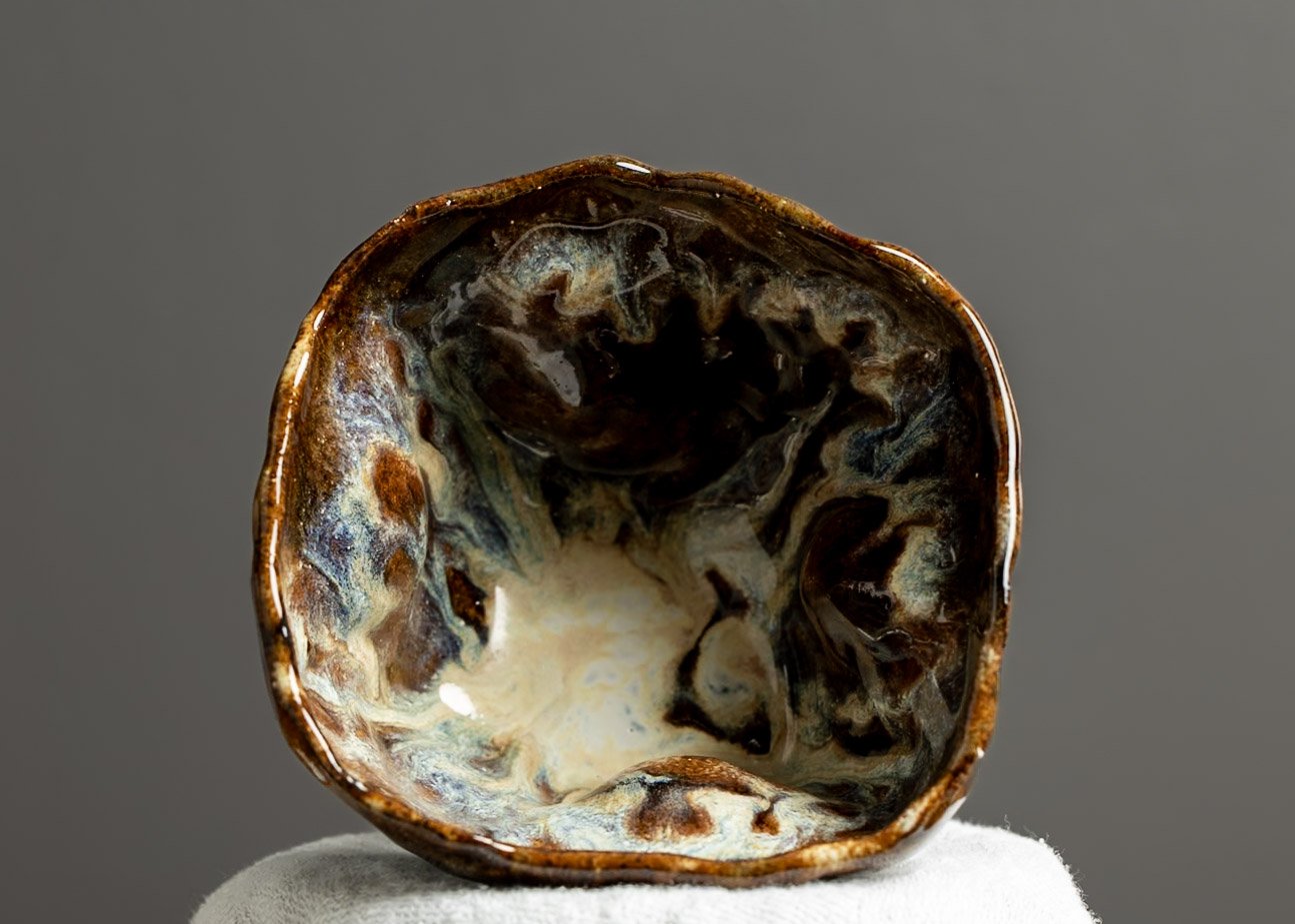 Close-up of an oyster shell with a glossy, multicolored interior, resting on a white surface against a plain gray background.