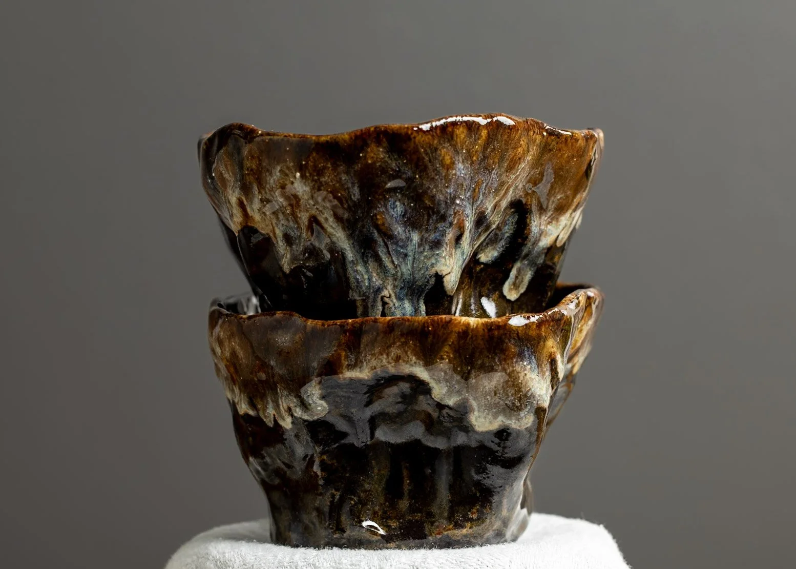 Two stacked ceramic bowls with a marbled brown and cream glaze on a white surface against a gray background.