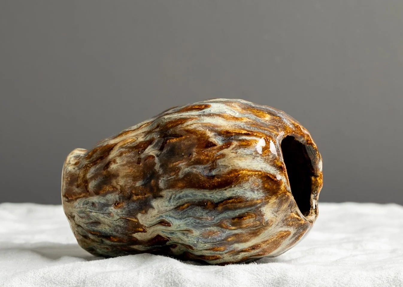 Charred, hollow pumpkin with a dark opening, lying on a white cloth against a gray background.