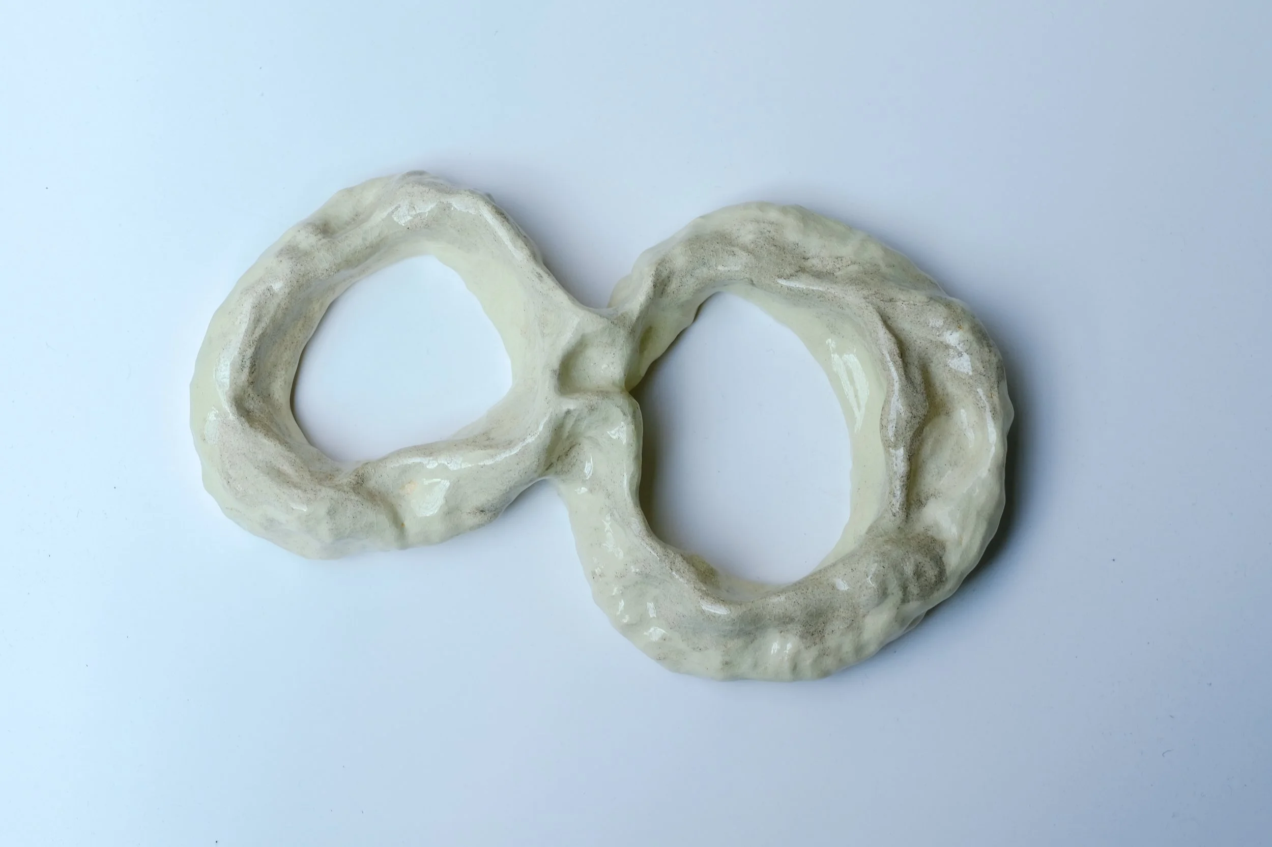 Two off-white, textured doughnuts arranged to form an infinity symbol on a white background.