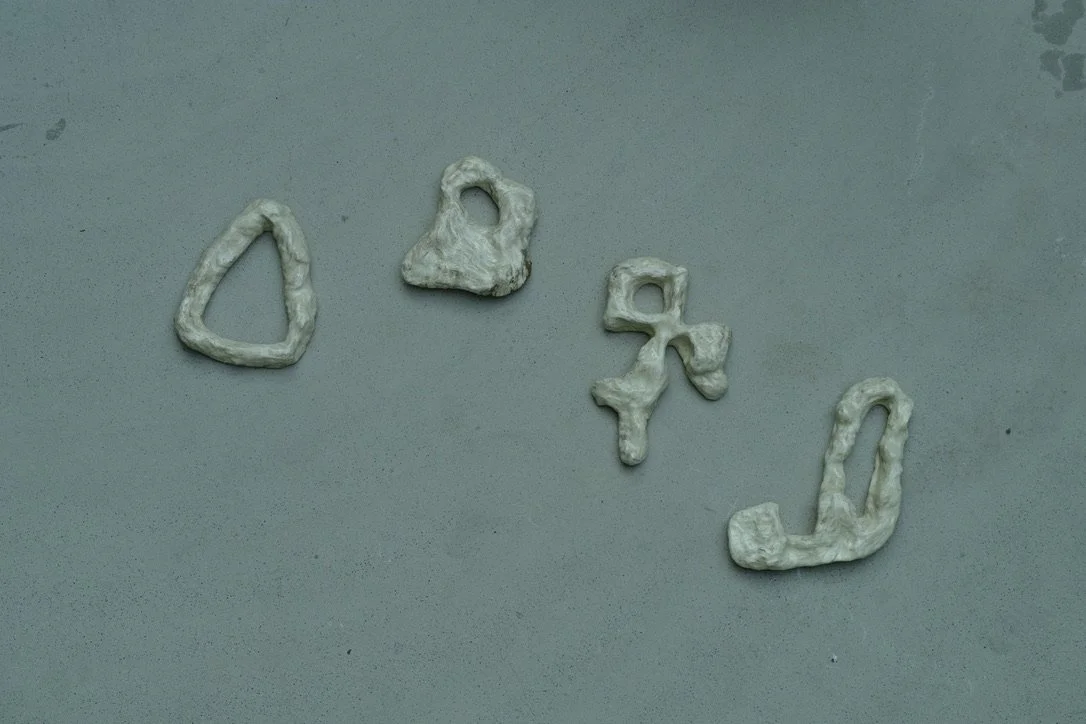 Four small, irregularly shaped, white objects resembling unassembled pieces or objects on a gray surface.