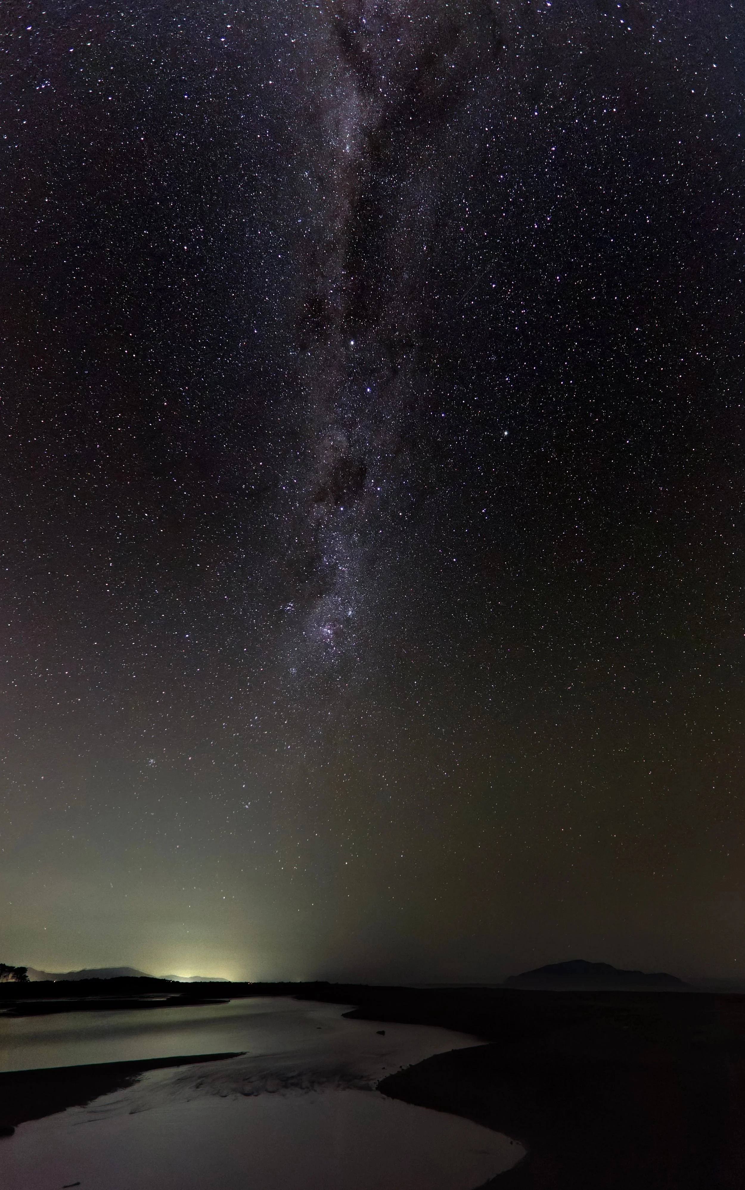 Night sky filled with stars and the Milky Way galaxy, with a river and distant hills in the foreground.