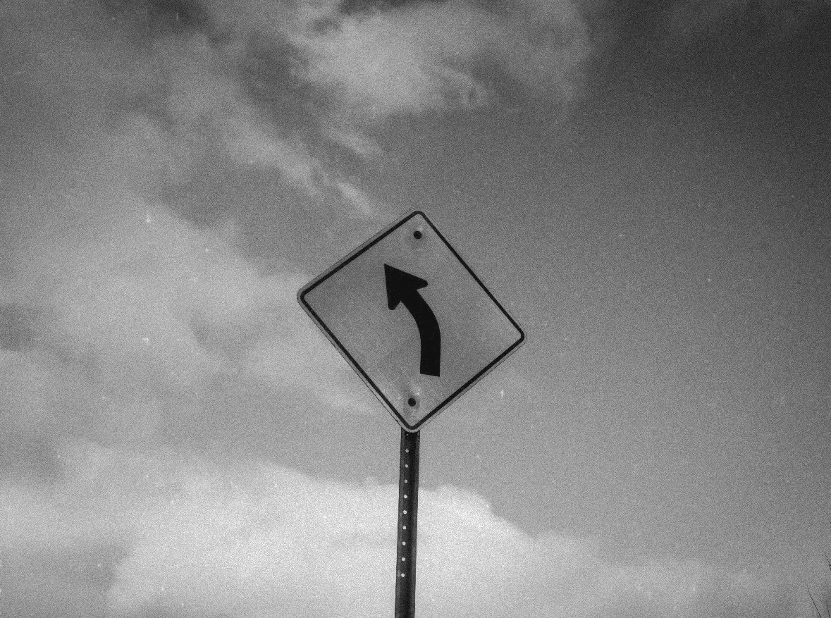 Black and white road sign indicating a left curve ahead