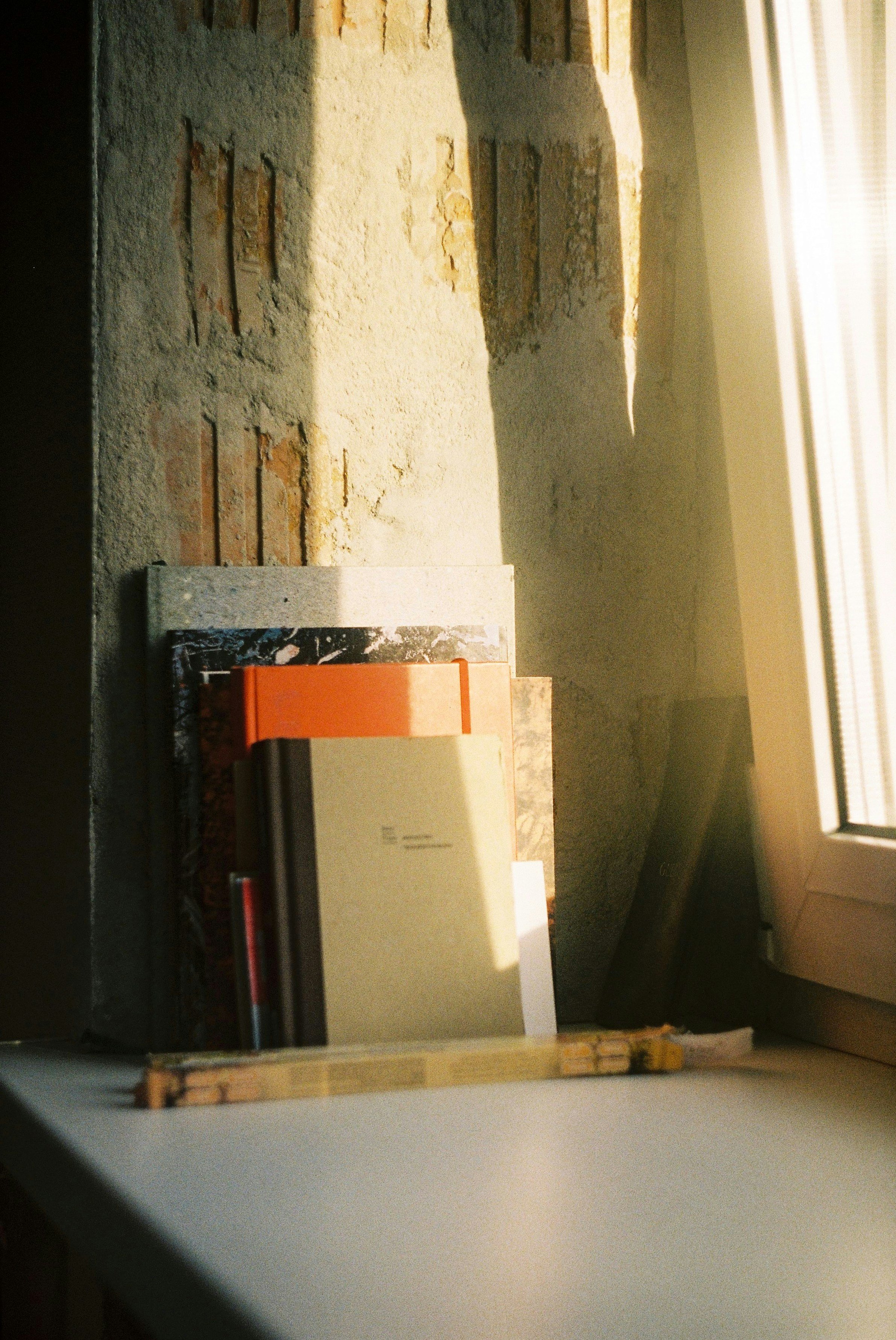 Books and a notebook on a white surface near a window with sunlight shining through.