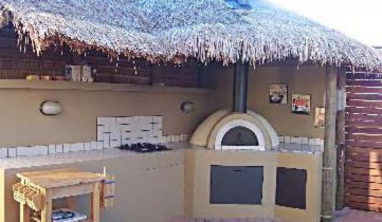Outdoor kitchen with a wood-fired pizza oven, a thatched roof, and a small wooden table.