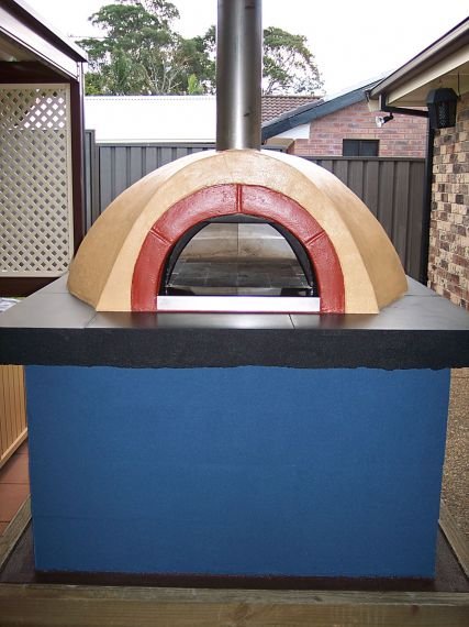 An outdoor pizza oven with a dome shape, featuring a red arch entrance, on a blue base, with a chimney pipe on top.