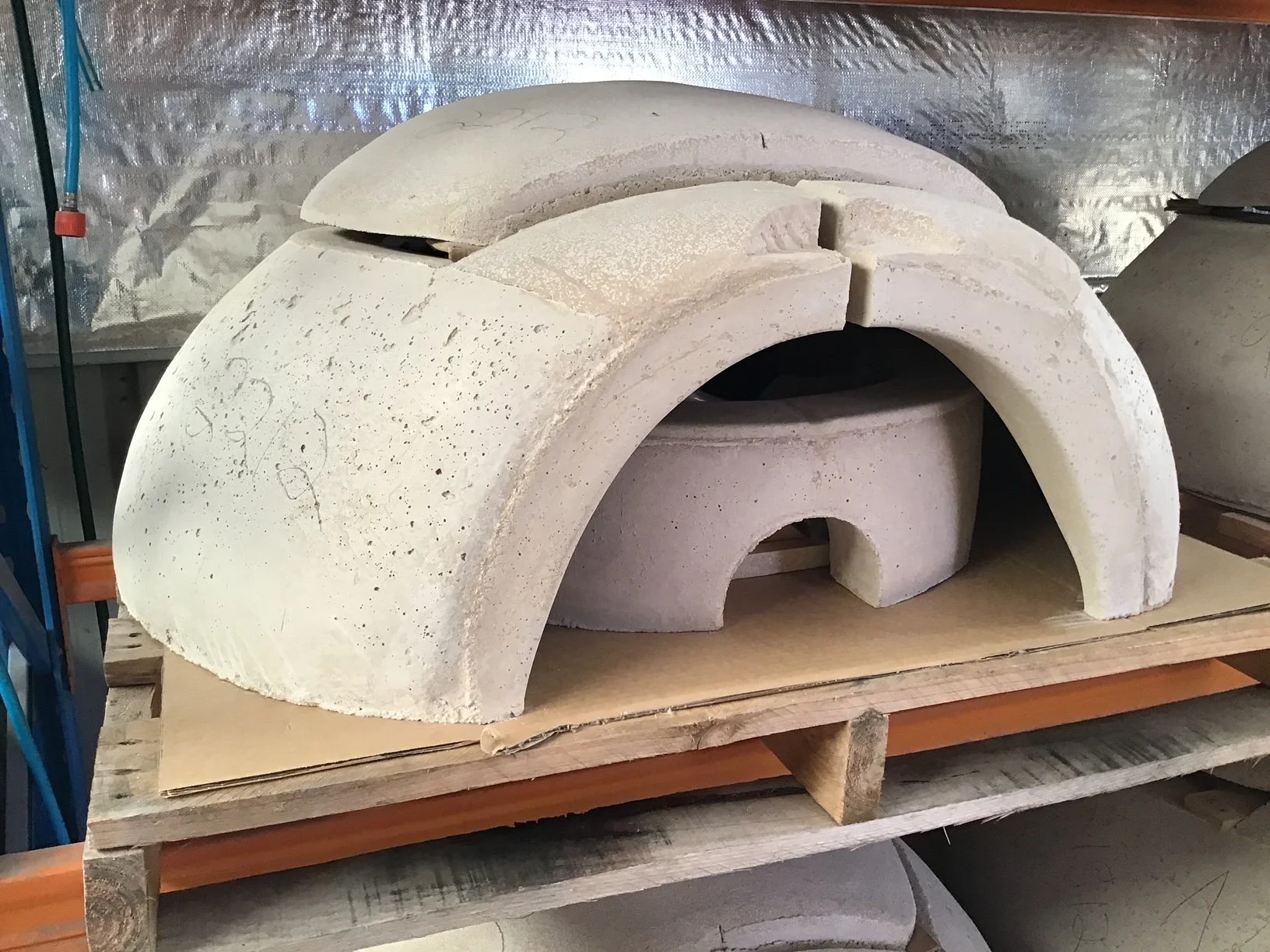 Unfinished concrete kiln or oven with arch-shaped openings on a wooden pallet in a workshop.
