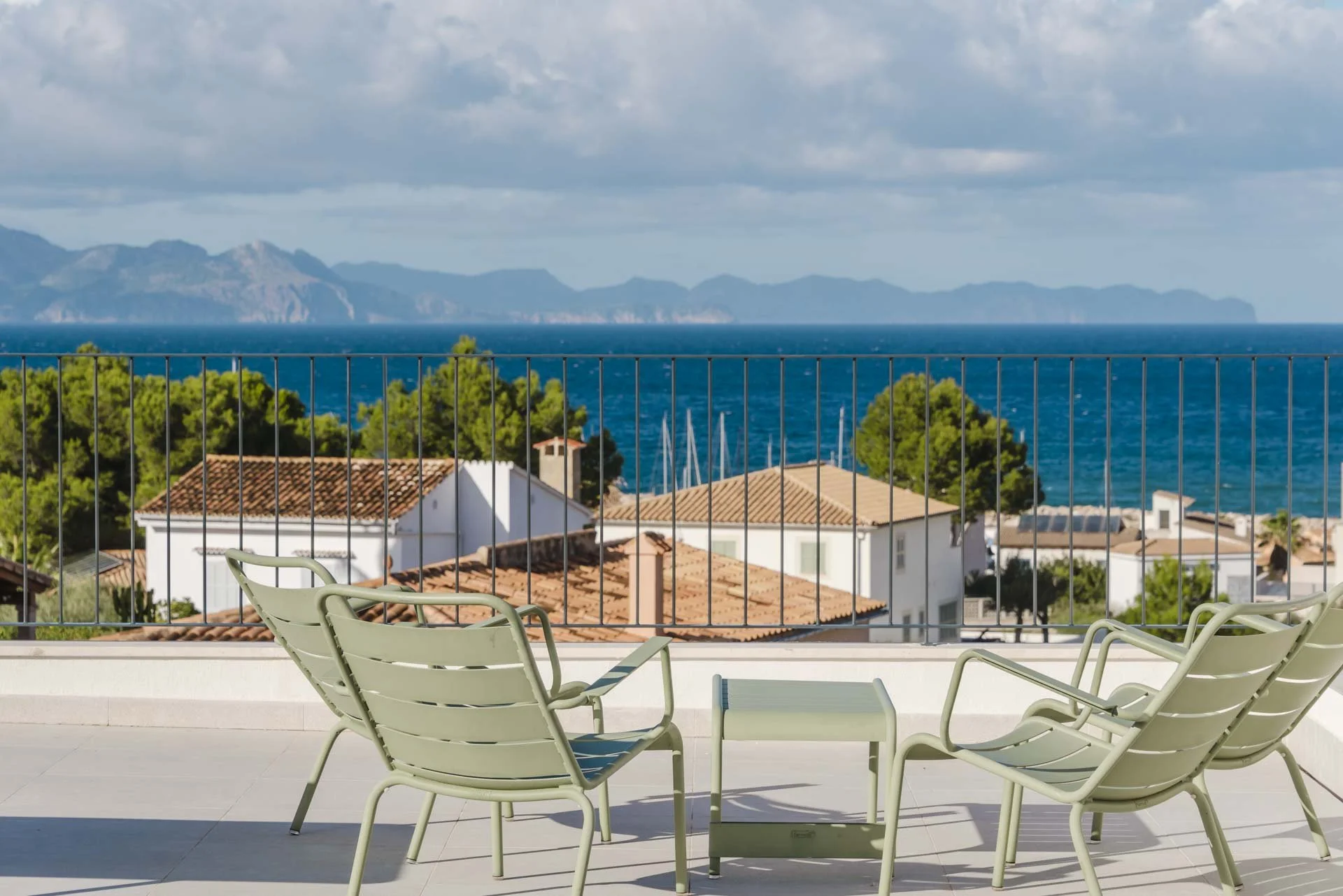 Porch with four white chairs and a small table overlooking rooftops, trees, ocean, and mountains in the distance.