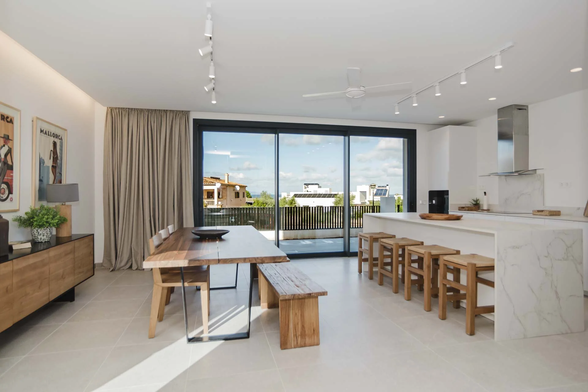 Modern open-concept kitchen and dining area with large sliding glass doors leading to a balcony, featuring wooden furniture, a white marble kitchen island, and decor items.