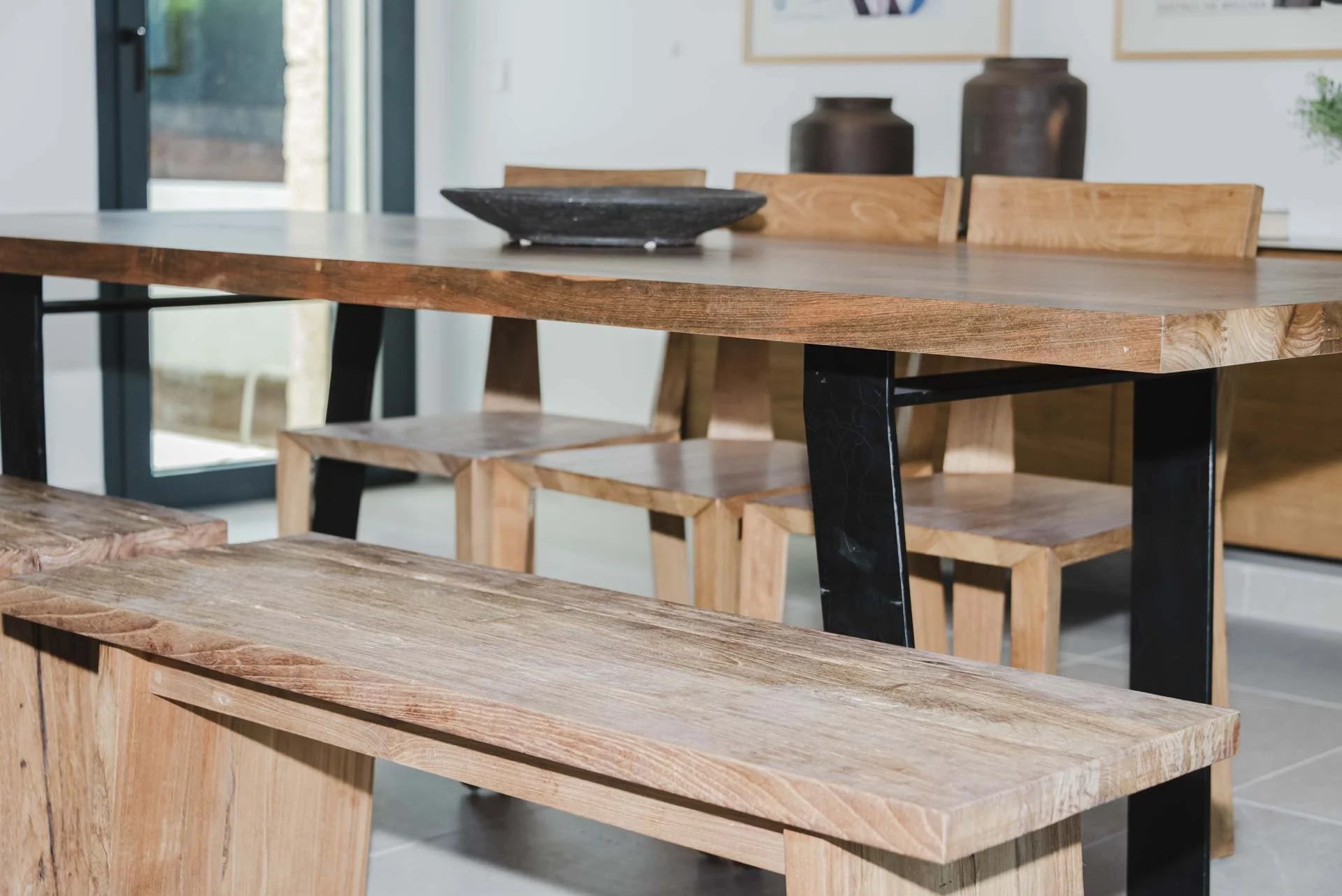 Interior of a dining room with a wooden table, wooden chairs, and decorative vases in the background.