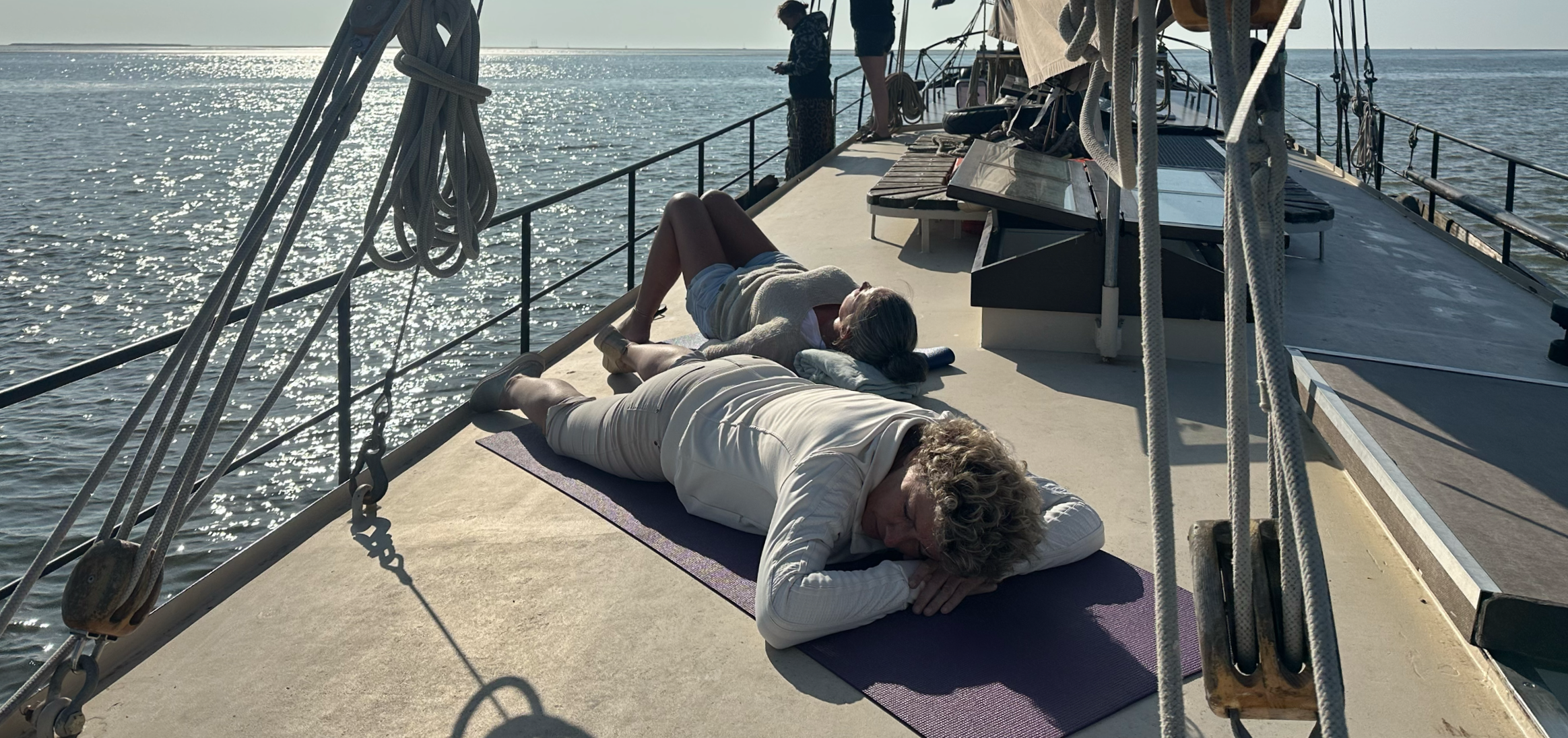 People practicing yoga and relaxing on a boat deck during sunset over the water.