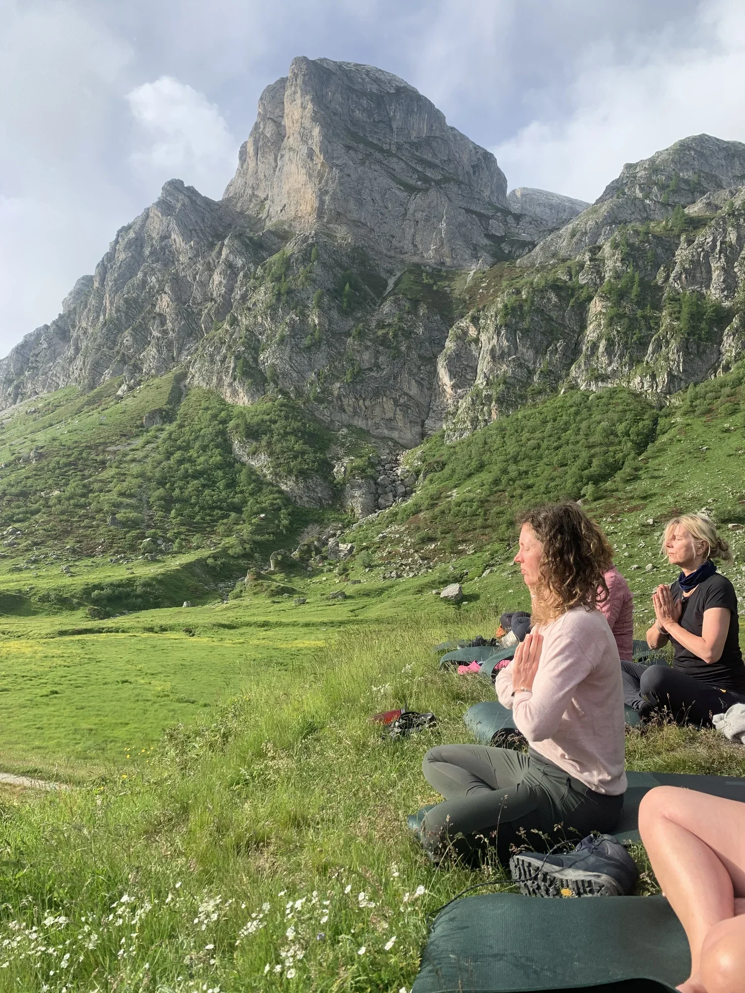 Group of women practicing yoga outdoors on a grassy field with mountains in the background.