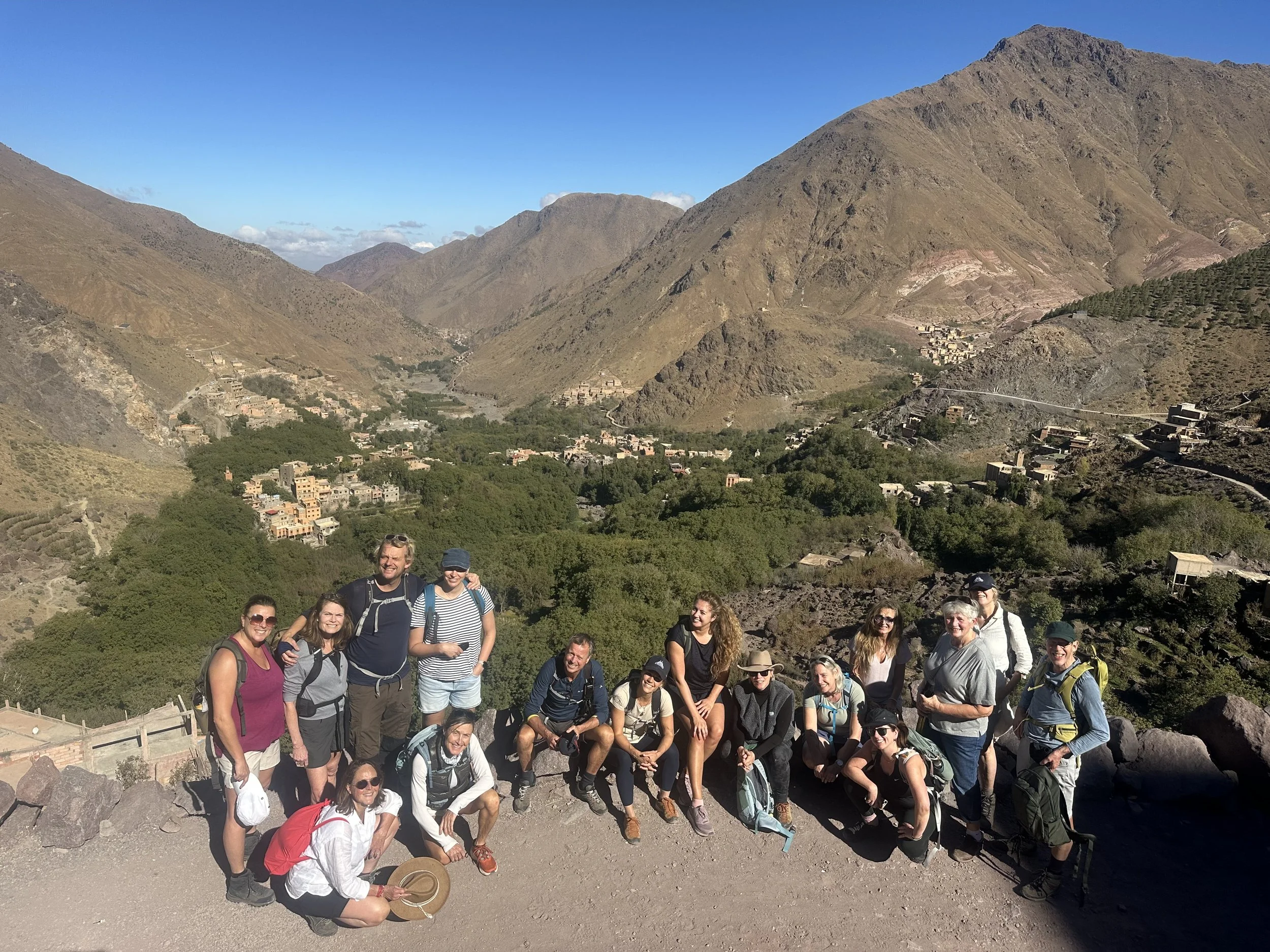 A group of people hiking in a mountainous area with a valley and scattered houses in the background.