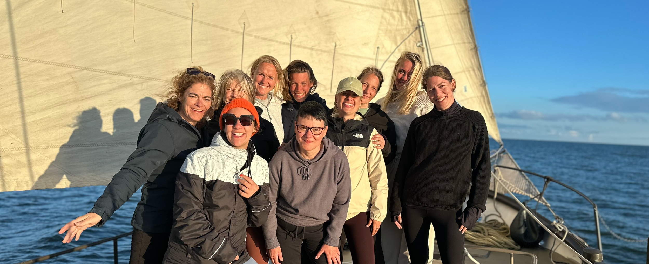 Group of women smiling on a sailboat with the ocean and blue sky in the background.