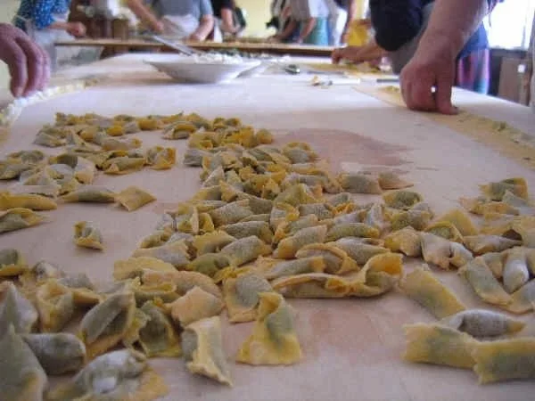 People making handmade pasta with scattered pasta pieces on wooden table.