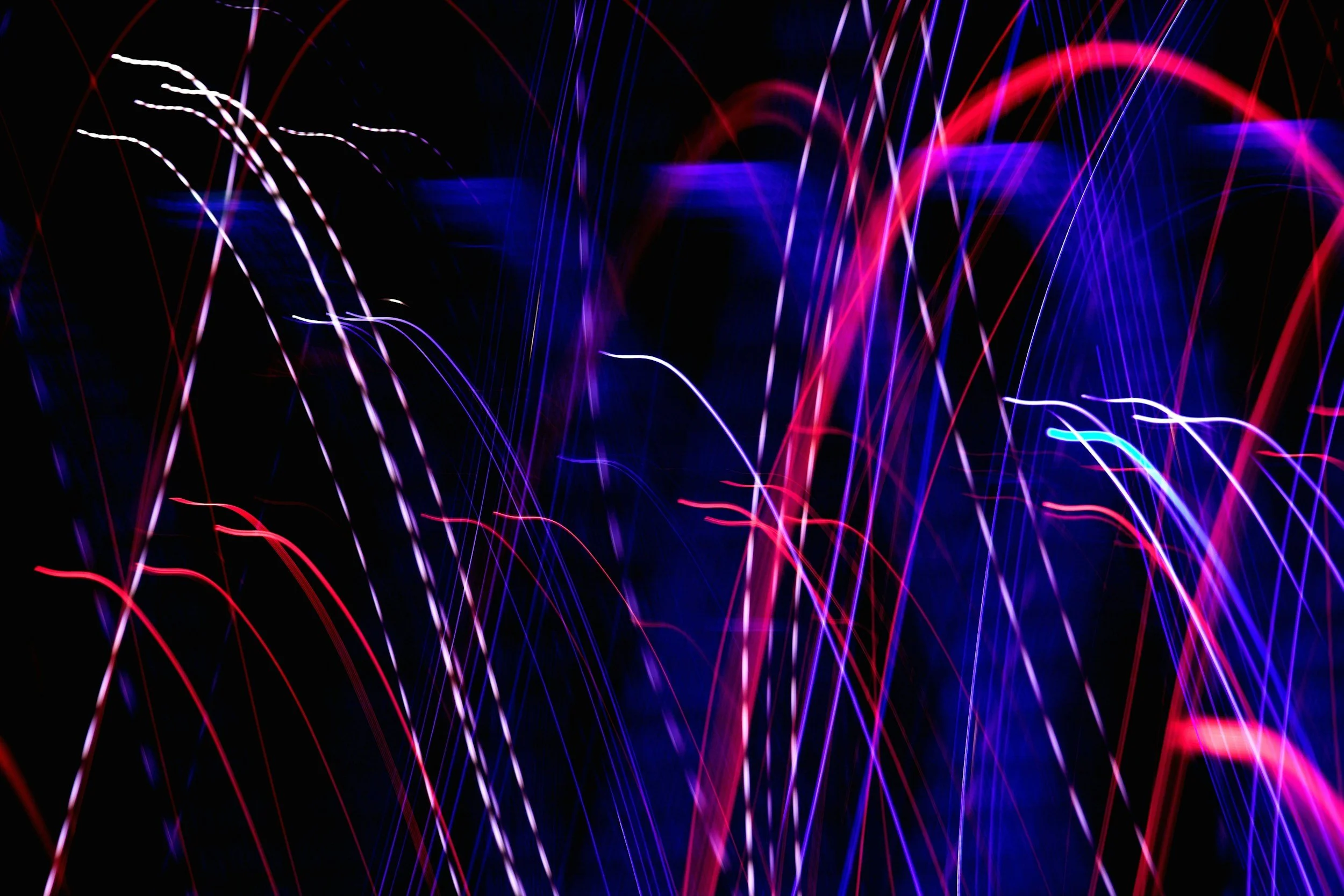 Colorful light trails in red, blue, purple, and white streak across a black background.