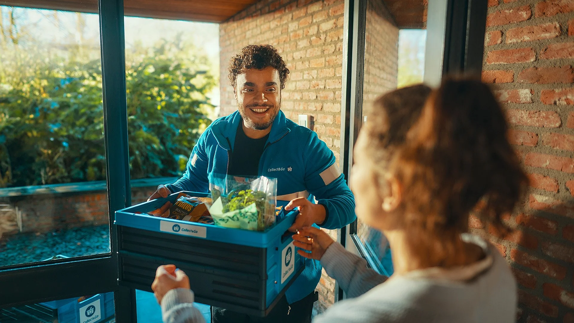 Collect&Go delivery driver hands a grocery crate to a woman at her front door