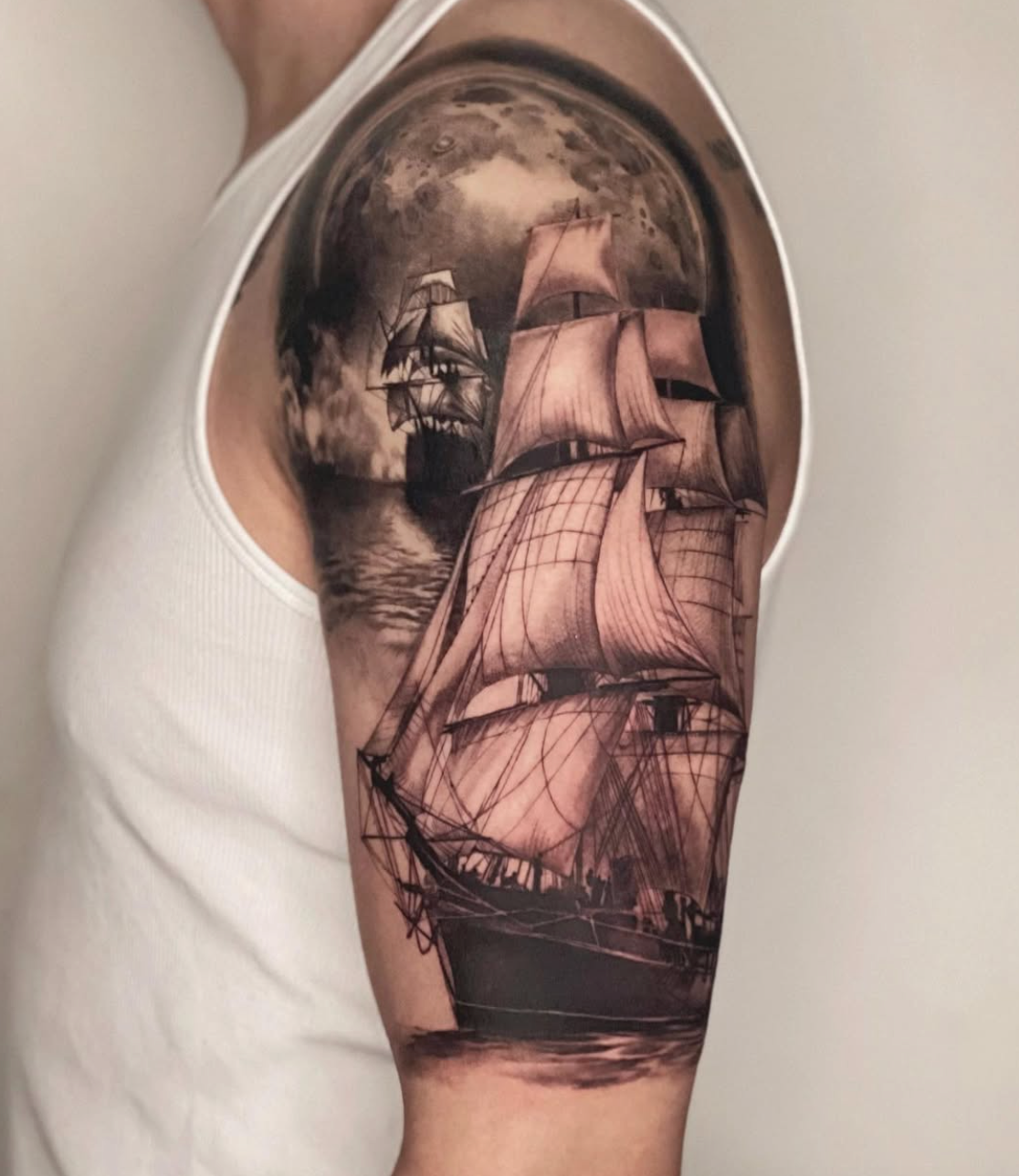 Tattoo of a ship sailing near the moon on a person's upper arm