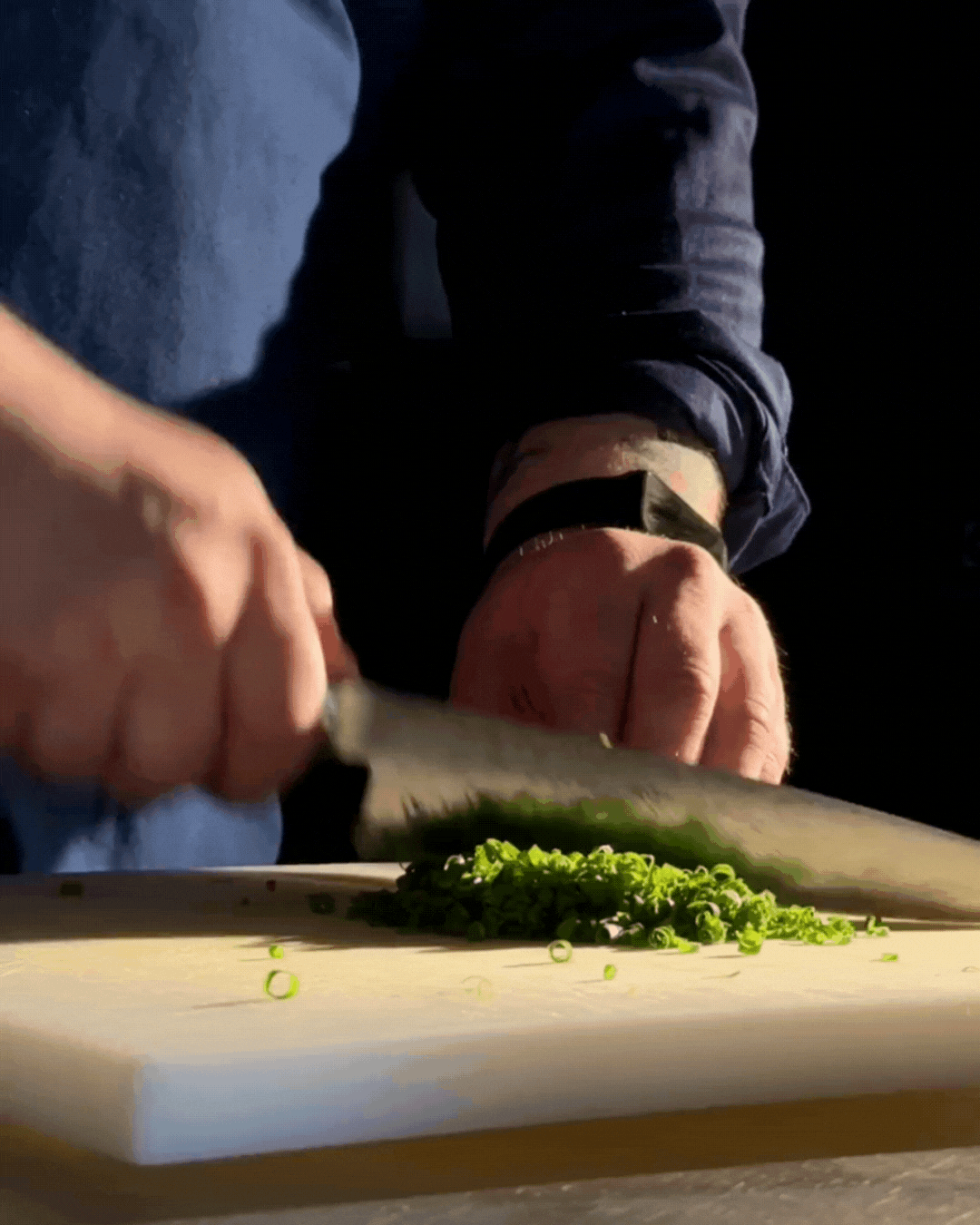 A person chopping green onions on a white cutting board in a kitchen.
