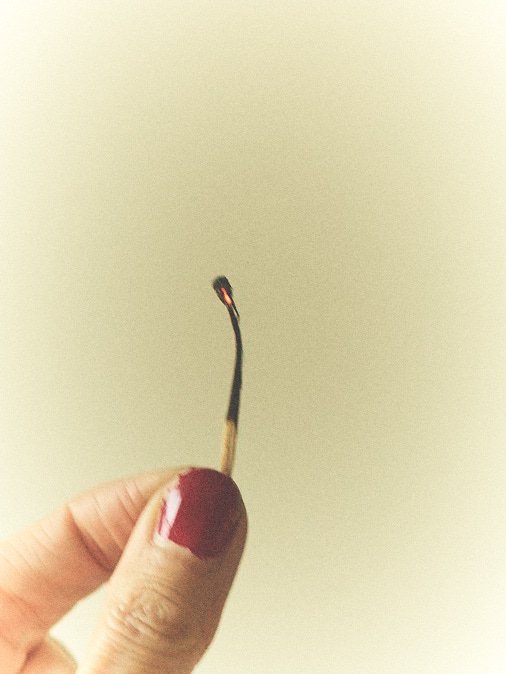 Close-up of a hand holding a lit matchstick with a small flame at the tip.