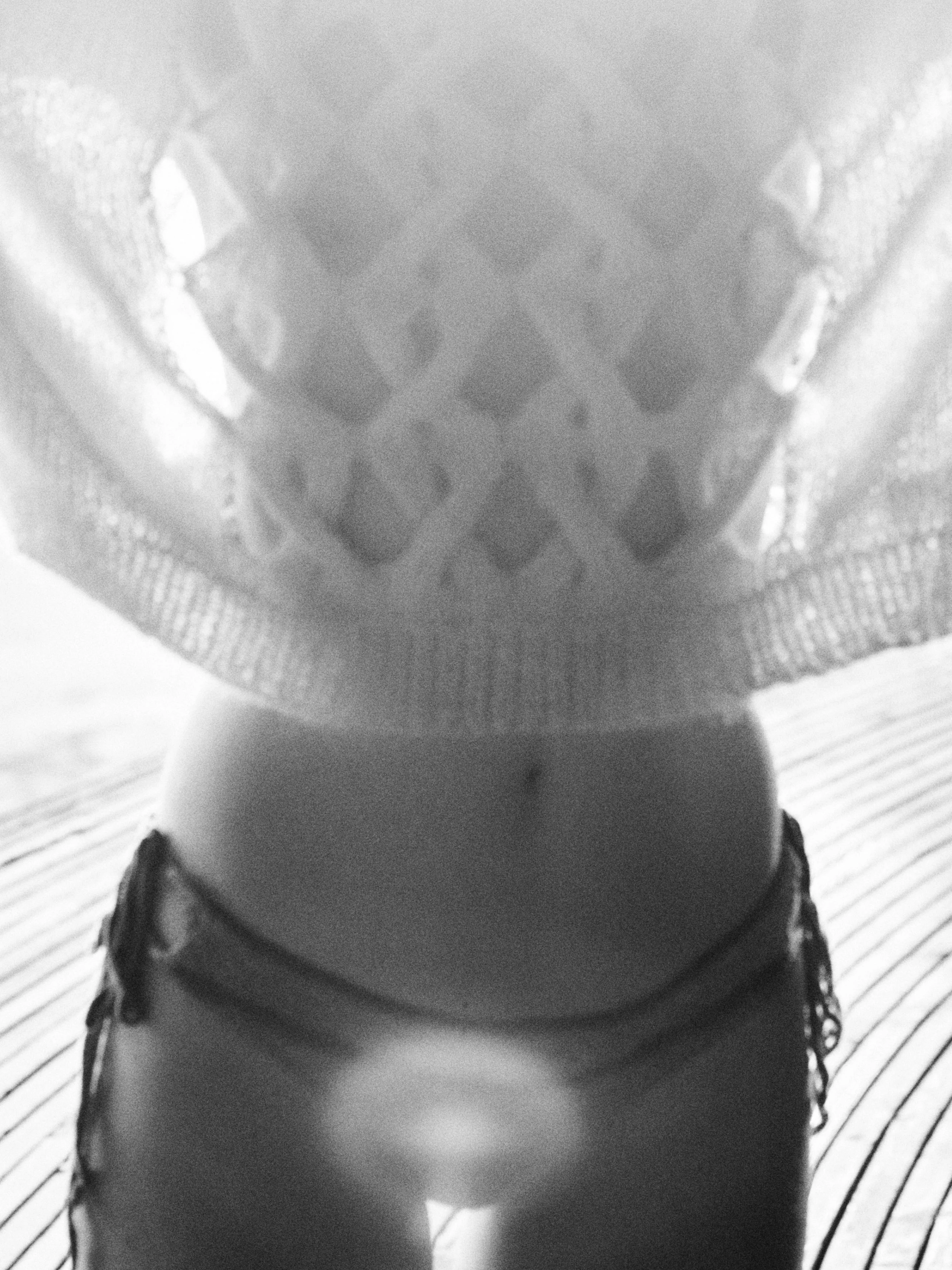 Close-up black-and-white photo of a woman’s waist and upper legs, wearing shorts, with a mesh top covering her midsection, standing on a wooden deck.
