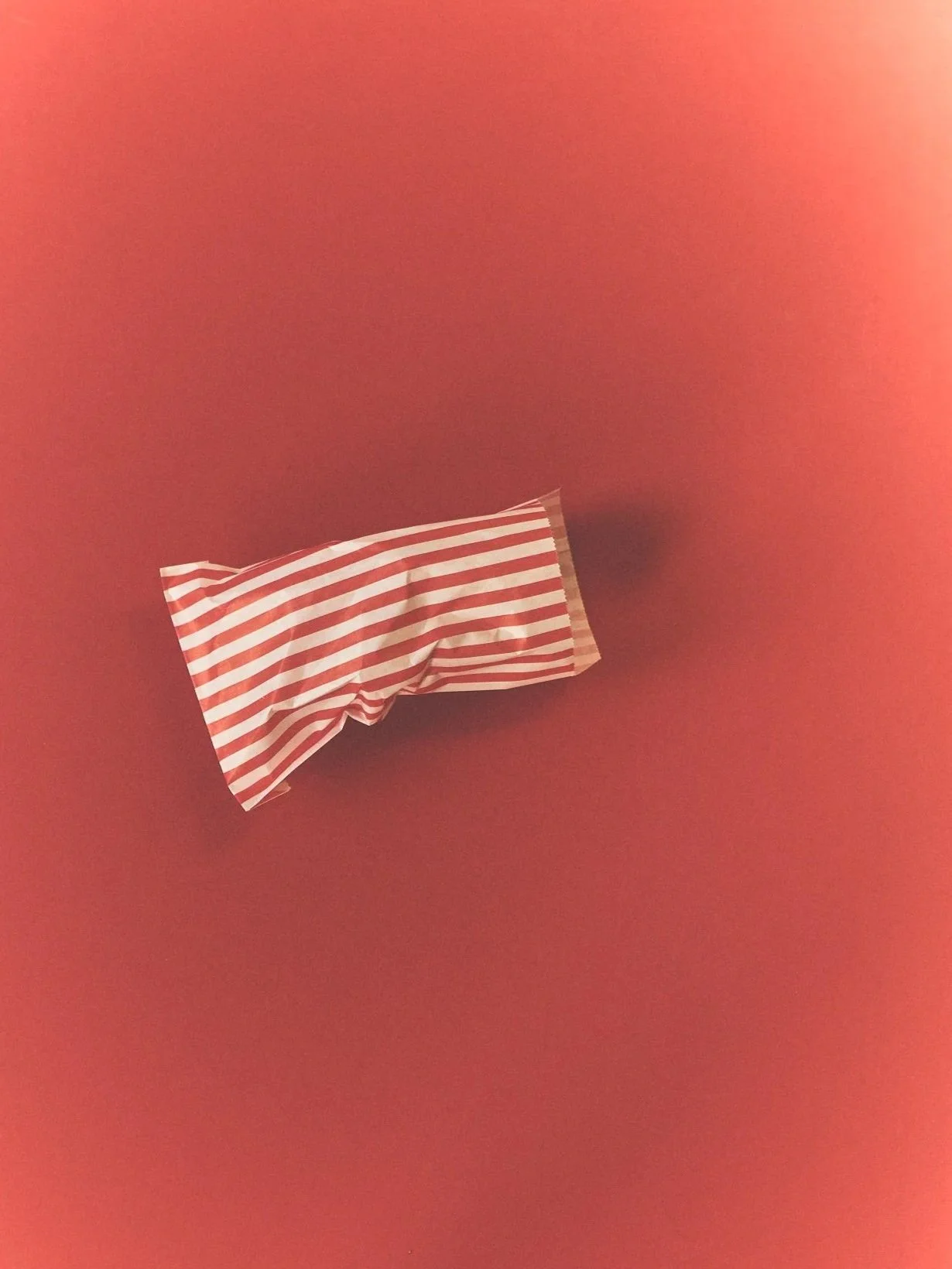 A crumpled piece of striped red and white paper on a reddish background.