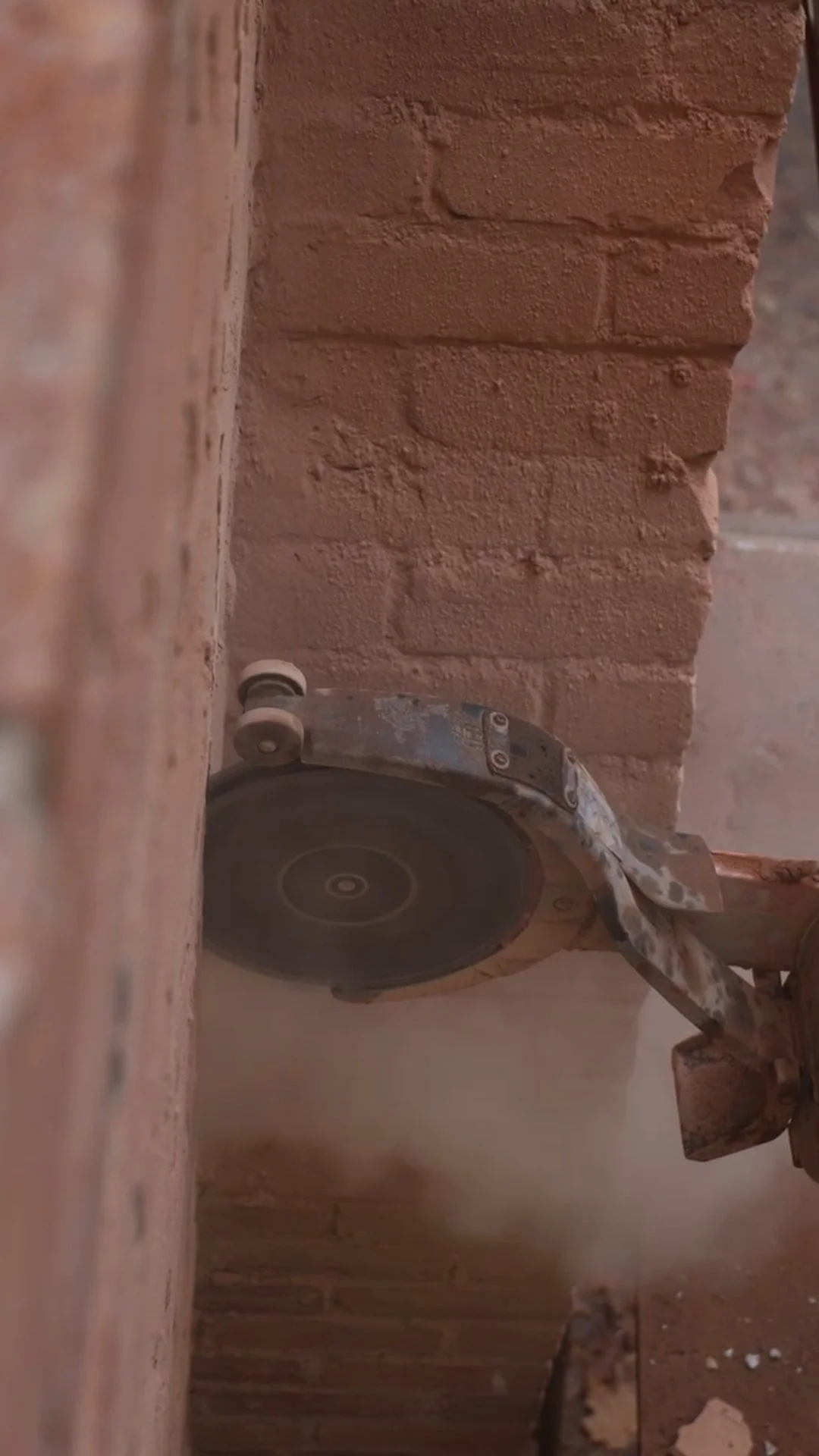 Close-up of a circular saw cutting through red brick wall.