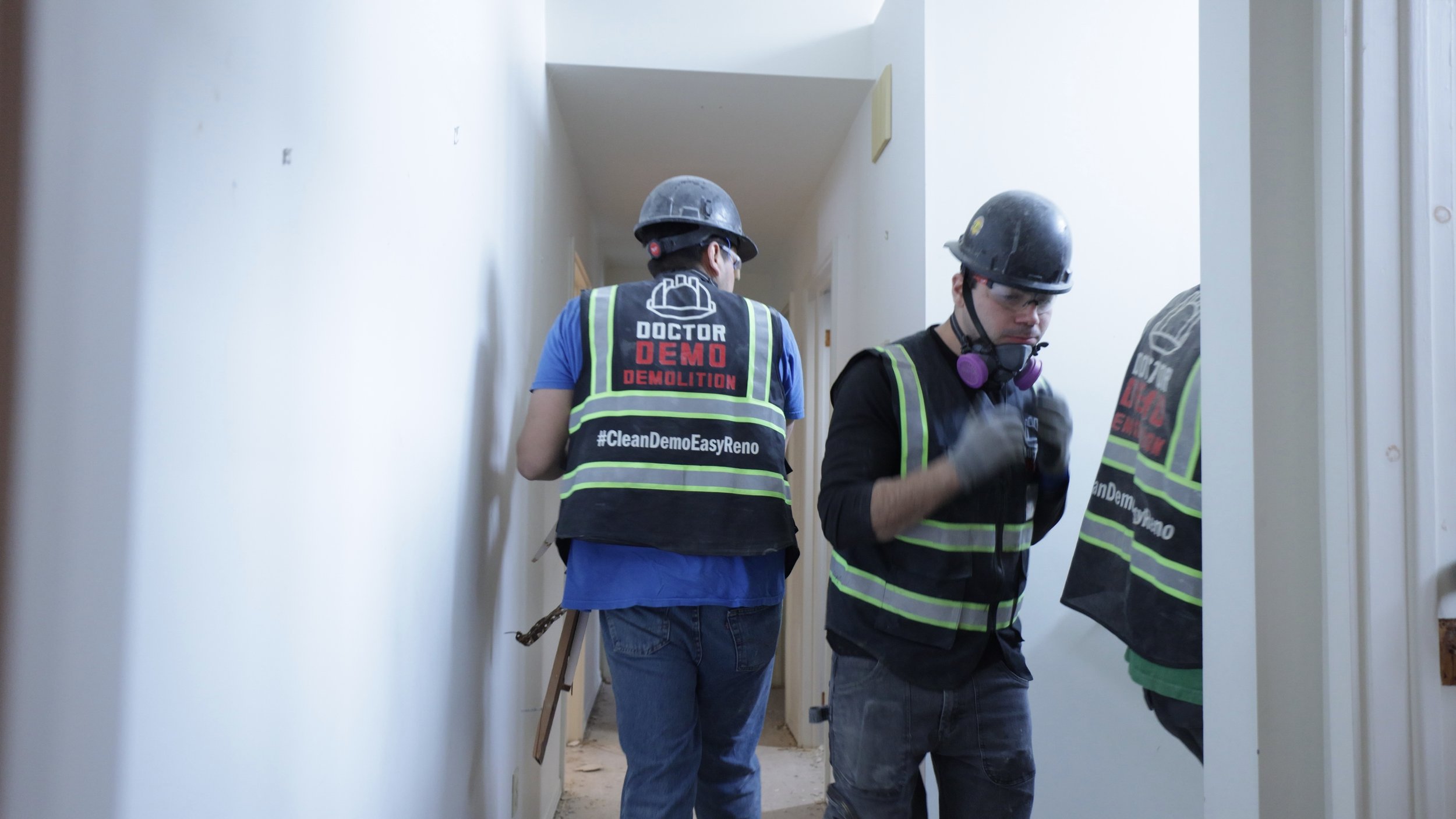 Two construction workers wearing hard hats and safety vests inspecting a hallway during a demolition project.