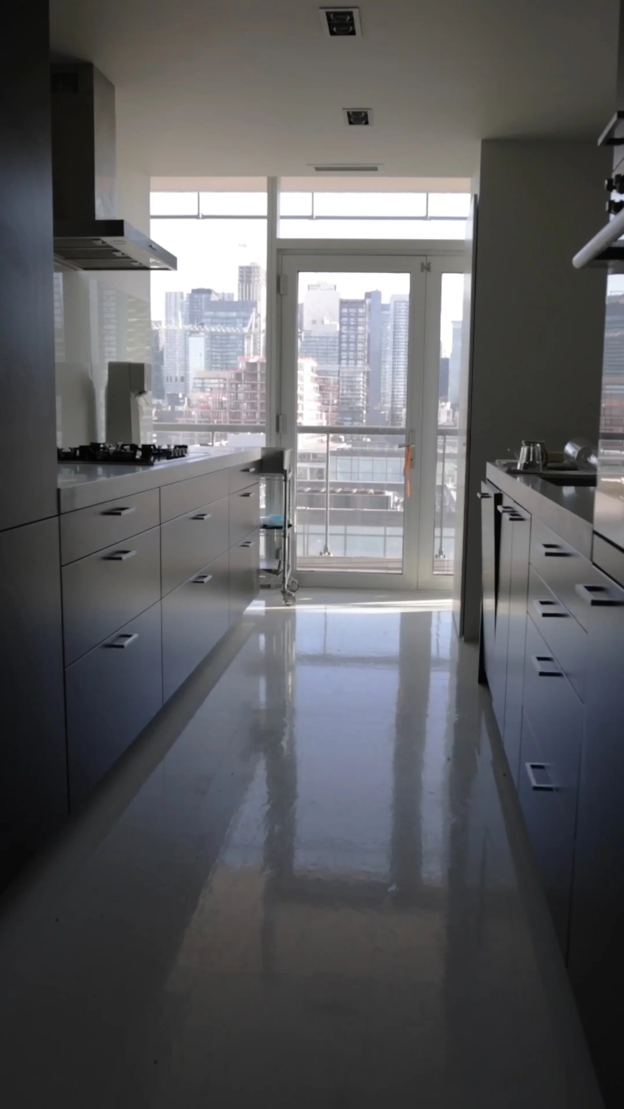 Modern kitchen with white cabinets, a black stove, and large glass windows showing a city skyline.