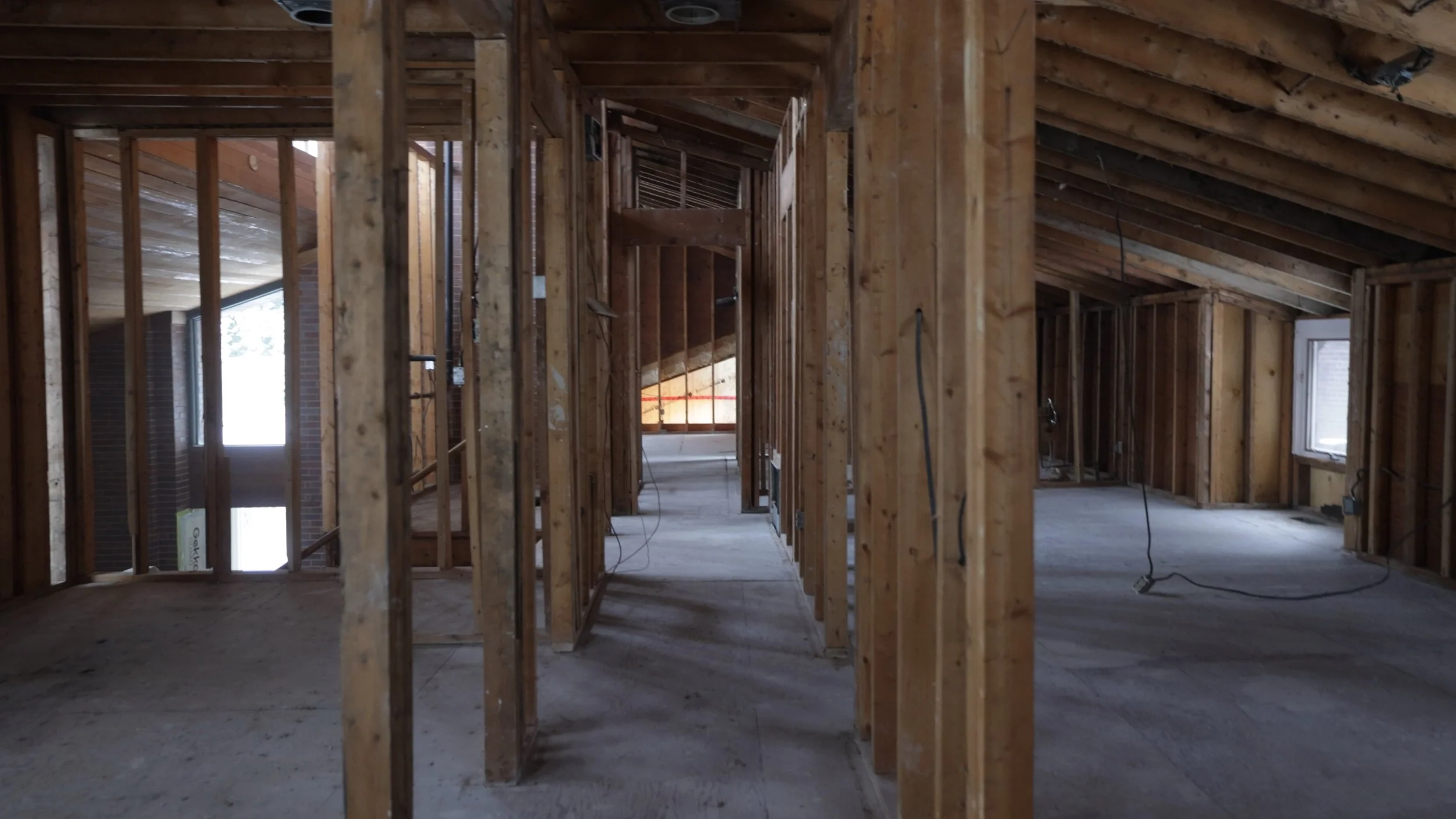 Interior view of a house under construction with wooden framing and a sloped ceiling, windows, and exposed wiring.