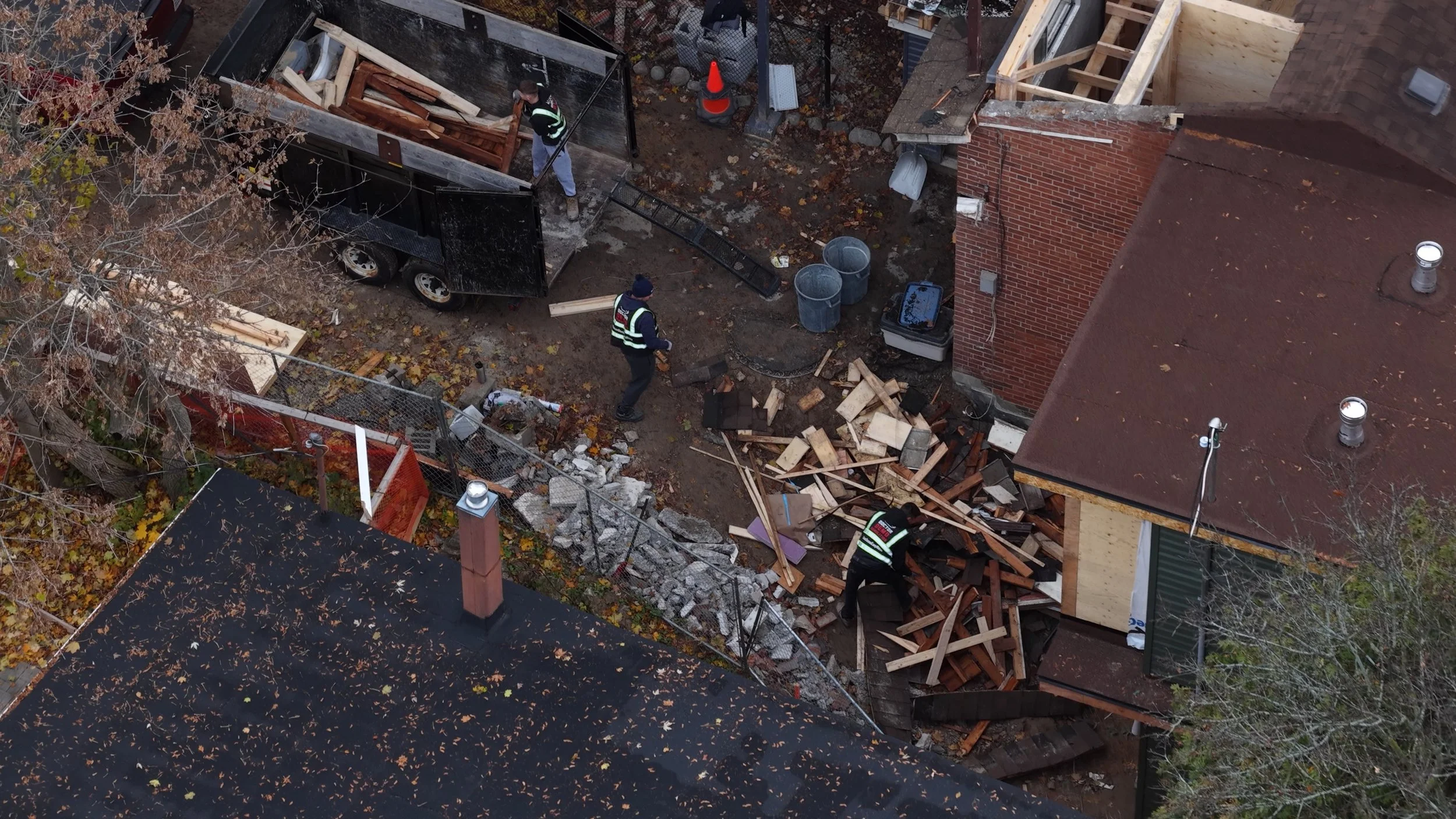 Workers demolishing and removing debris from a backyard construction or renovation project, surrounded by scattered wood, bricks, and construction equipment.