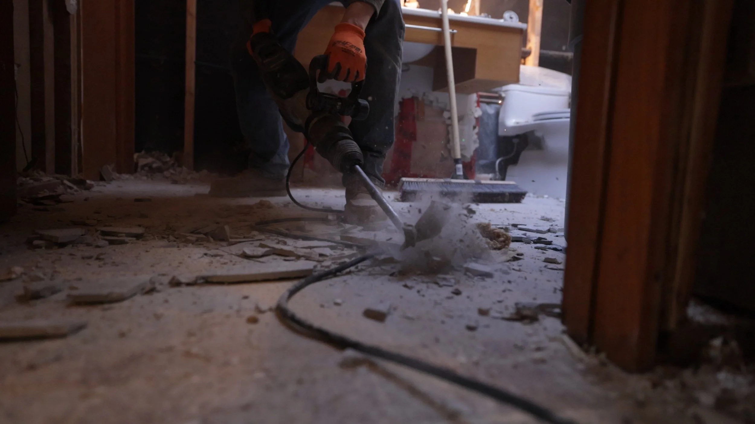 Worker using a jackhammer to break up concrete floor inside a partially constructed building.