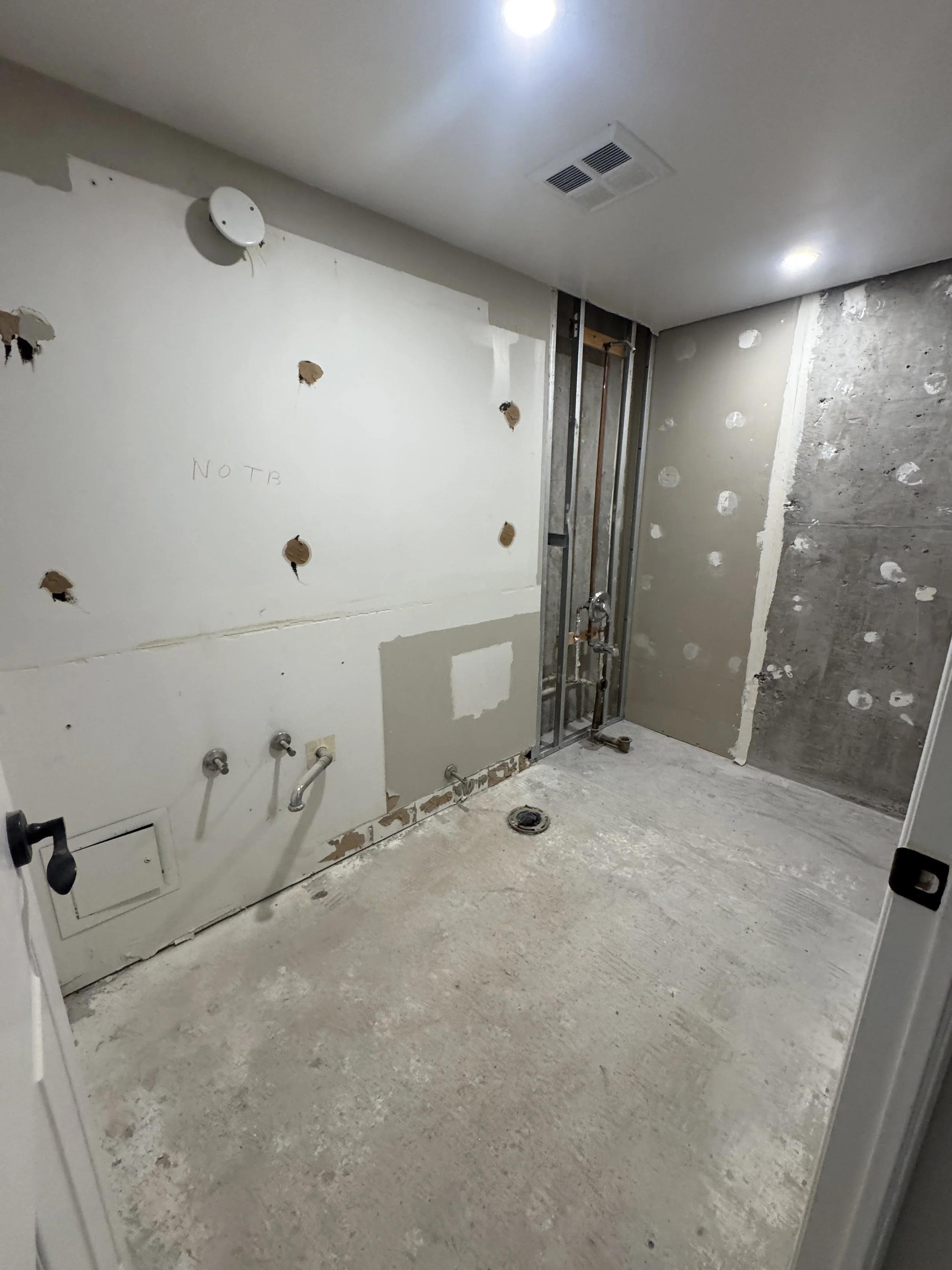 Interior of a room under renovation with exposed drywall, plumbing, and unfinished wall surfaces.