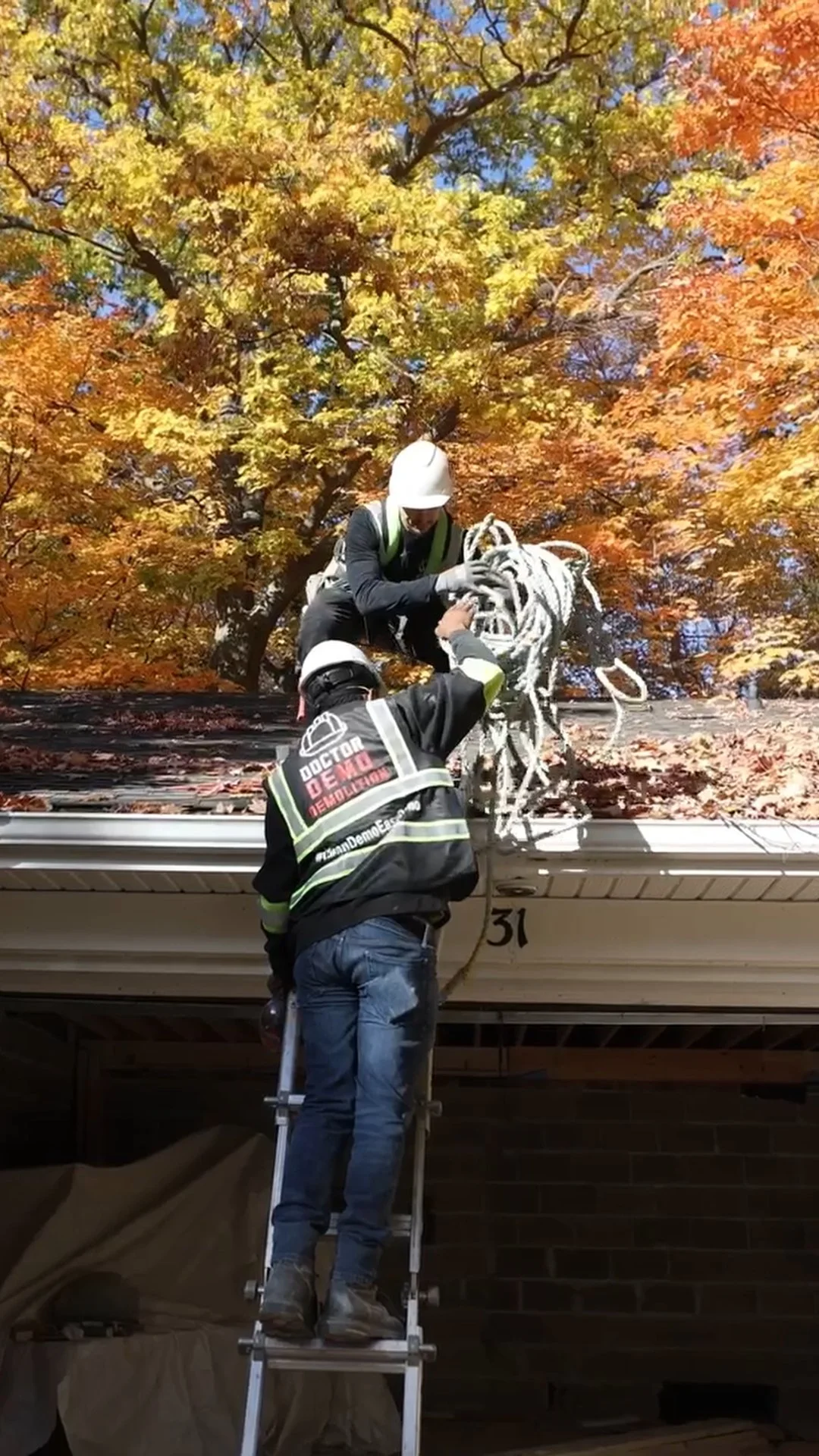 Firefighters installing or maintaining equipment on a house roof during autumn, with colorful fall foliage in the background.