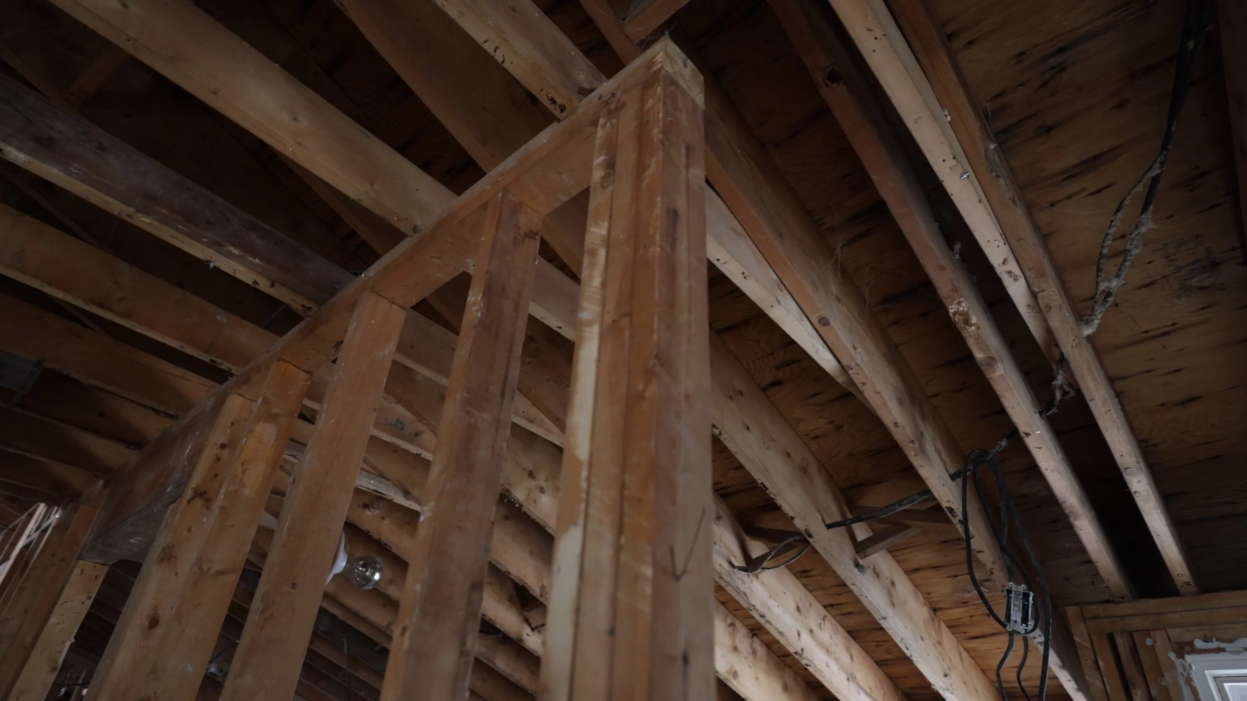 Interior view of a building under construction, showing wooden framing and exposed ceiling joists.