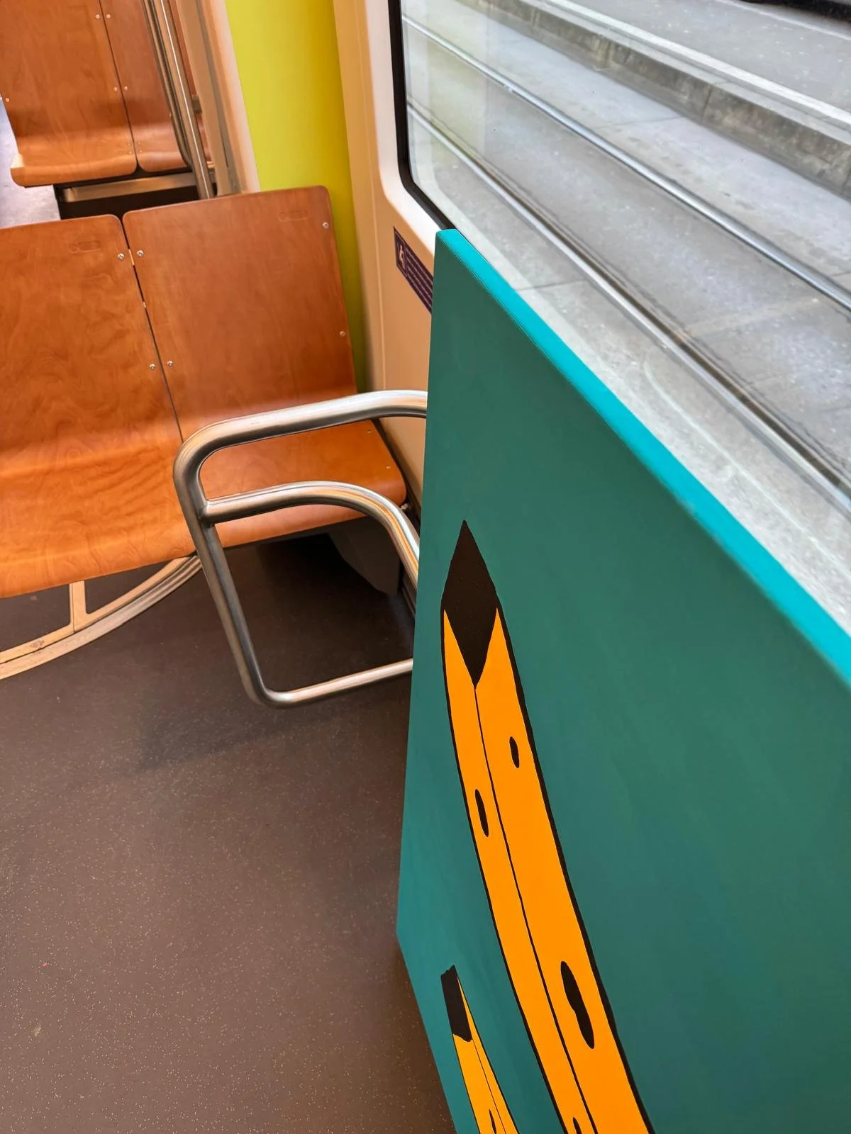 Innenraum eines Zuges mit Holzsitzen, ein gelber Koffer und ein Fenster mit Blick auf Eisenbahnschienen.