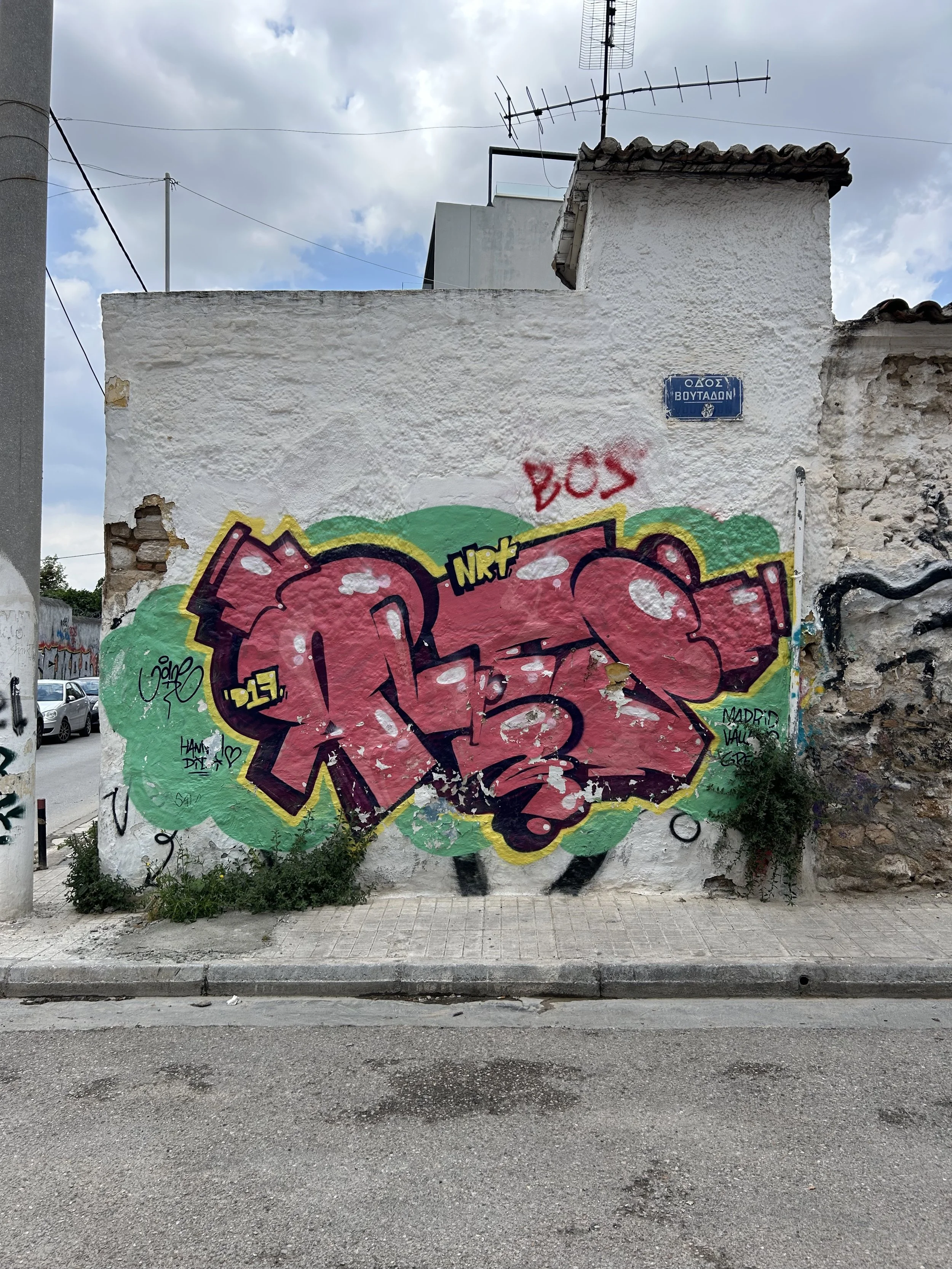 Graffiti auf einer weißen Hauswand mit grünen und rosa Elementen, im Hintergrund Himmel und eine Straße