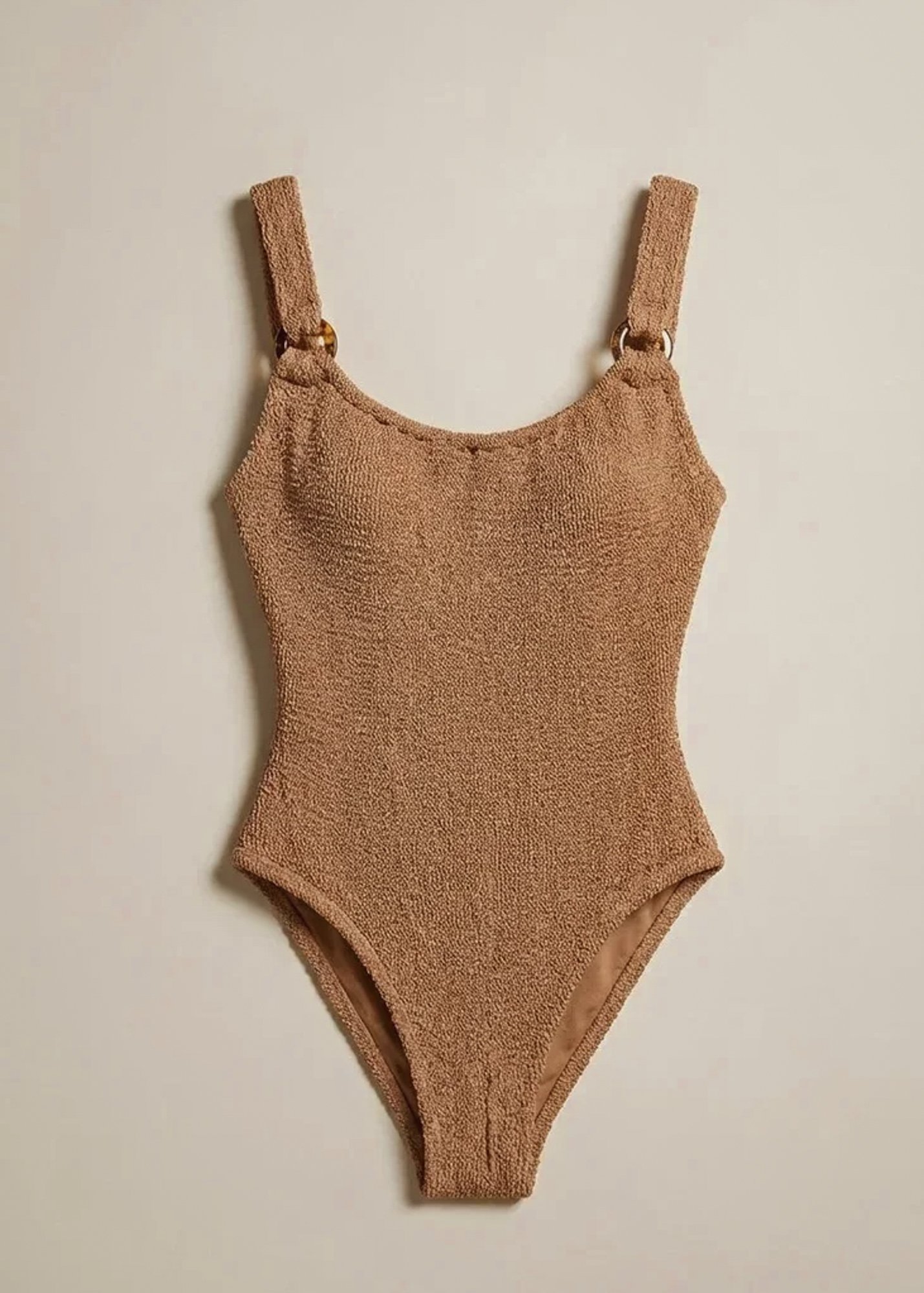 A tan textured one-piece swimsuit hanging on a wall.