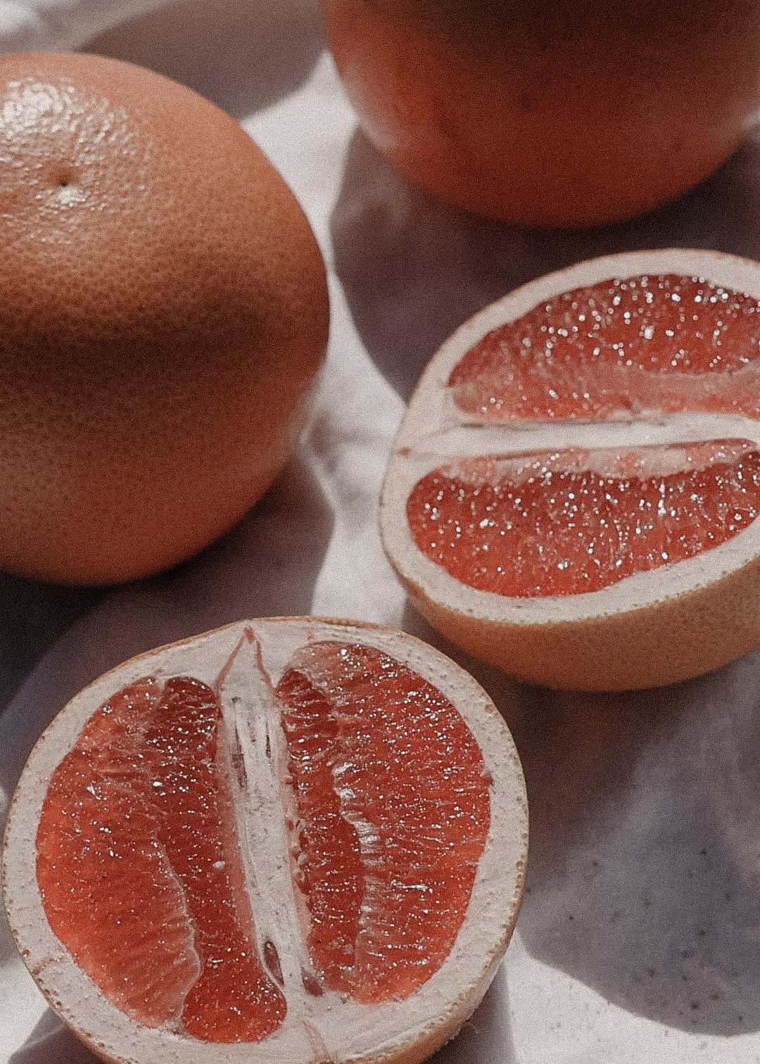 Close-up of whole and halved grapefruits on a flat surface.