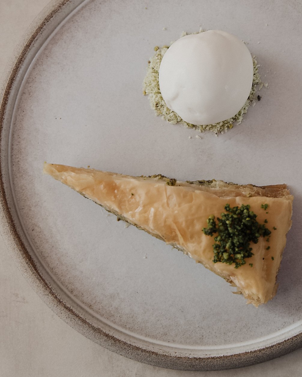A slice of salmon tart with a sprig of herbs on top and a scoop of ice cream or sorbet on a white plate.