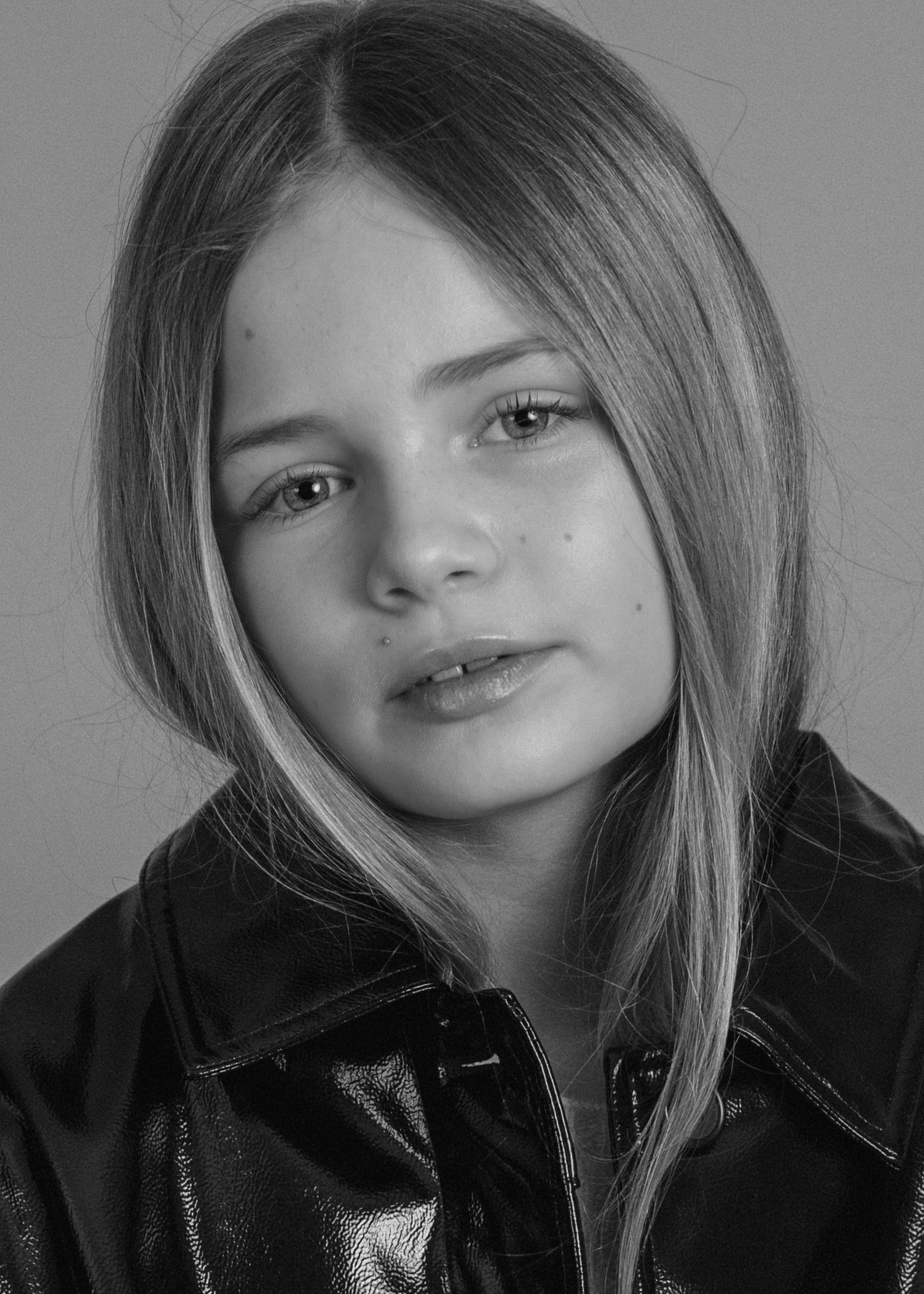 Black and white portrait of a young woman with straight hair, wearing a leather jacket, looking at the camera with a slight smile.