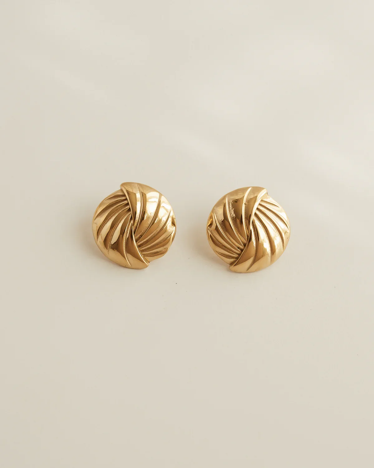 Pair of gold twisted knot earrings displayed on a plain, light-colored surface.
