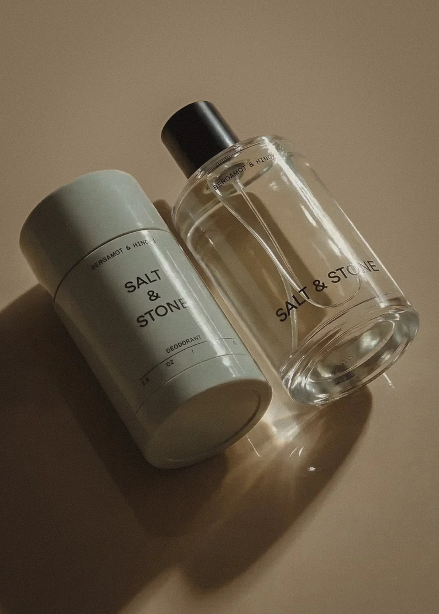 A white salt and stone deodorant container and a clear salt and stone spray bottle with black cap, both labeled 'Salt & Stone'.