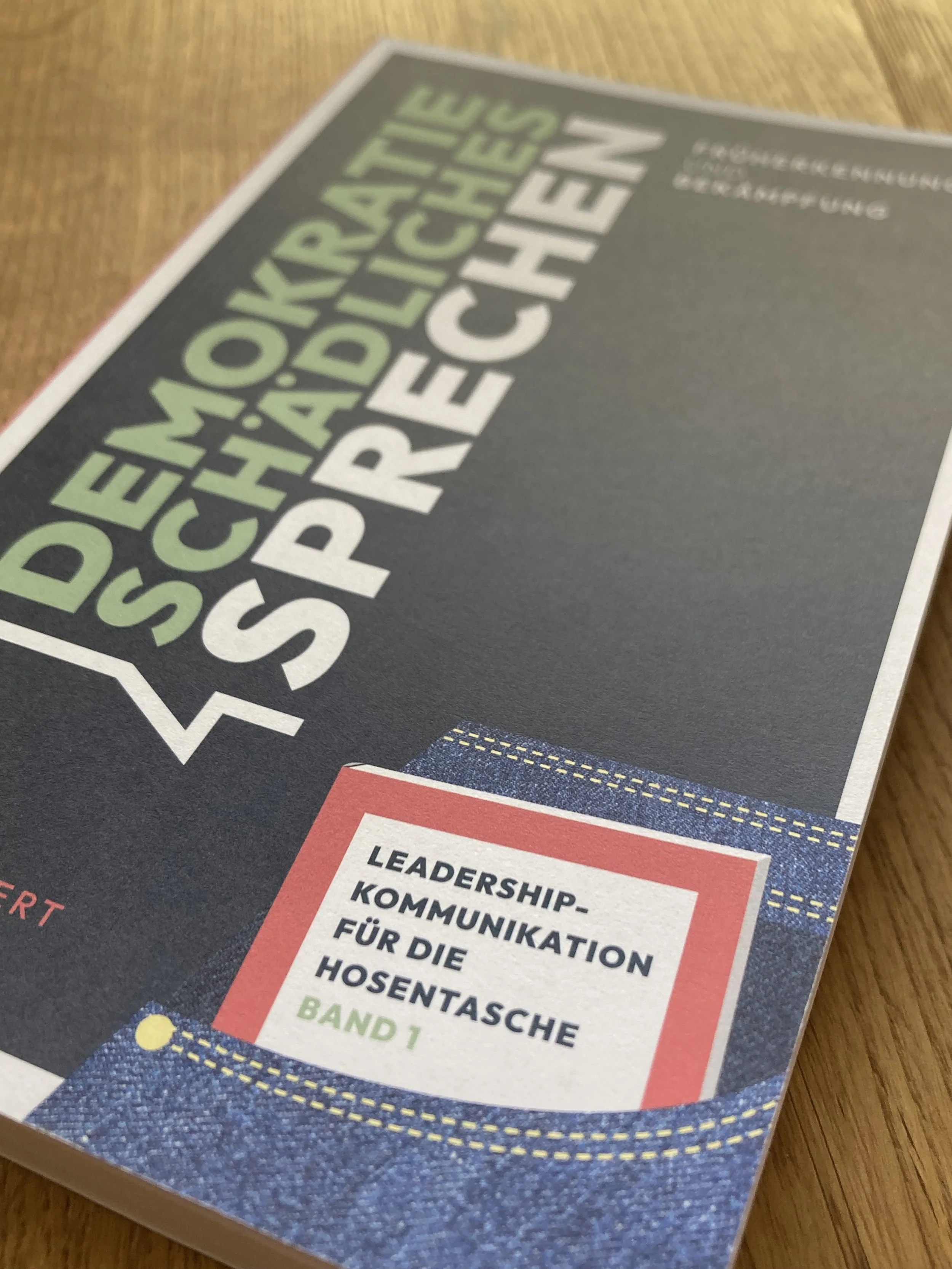 Buchcover mit dem Titel 'Demokratieschädliches Sprechen' und einem roten Buch in einer Hosentasche mit Text 'Leadership-Kommunikation für die Hosentasche Band 1'.