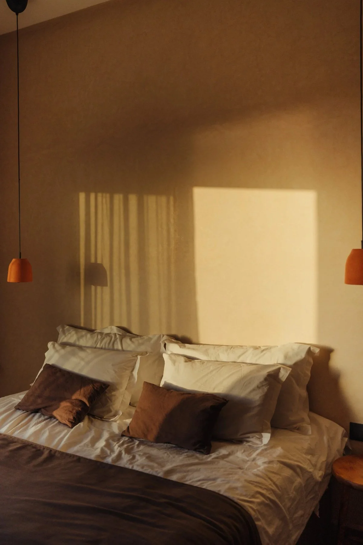 Cama con cojines en tonos naturales y luz cálida.