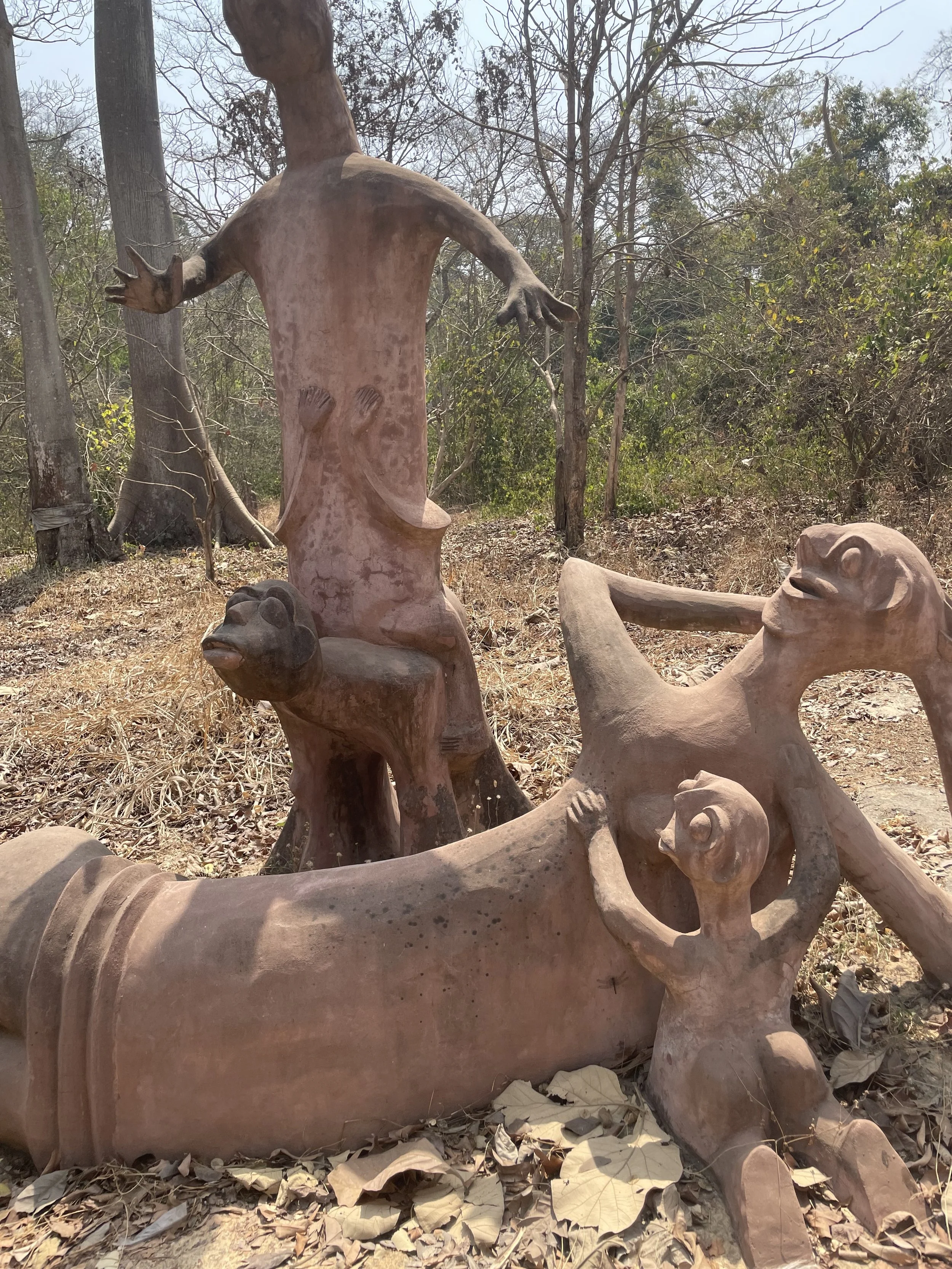 Scattered sculpture of various animal figures including a monkey, with a large tree and sparse forest in the background.