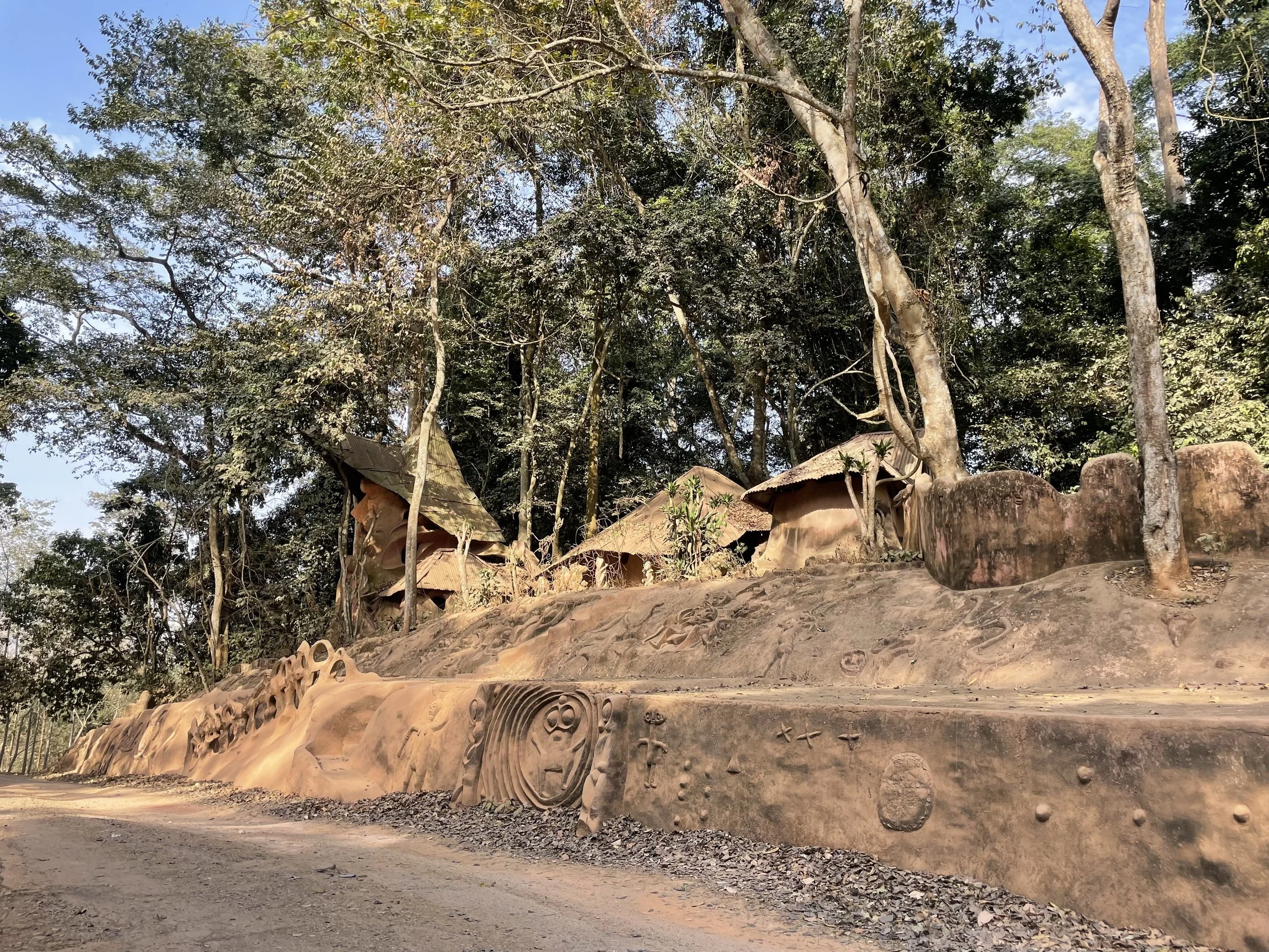 Clay sculptures and carvings on a hillside surrounded by trees, with some structures resembling small huts or houses.