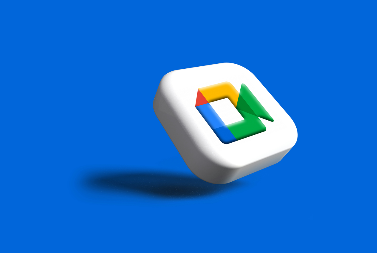 The image shows the logo for Google Meet, which appears as a three-dimensional, rounded white square icon. Inside the white icon is the video call symbol colored with Google's brand colors: yellow, red, and blue forming a stylized house shape, and a 