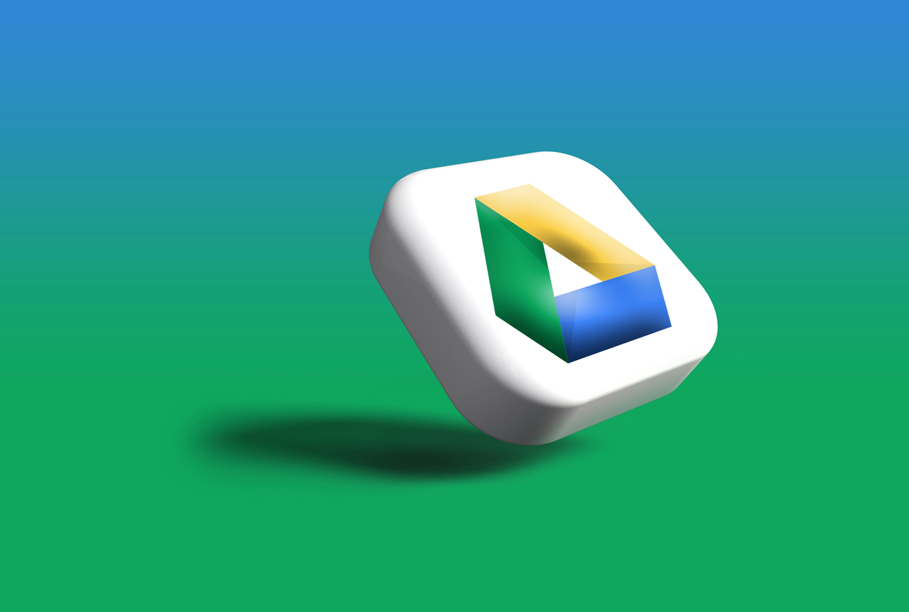 The image shows a 3D rendition of the Google Drive logo floating in front of a blue and green gradient background. The logo is a white, rounded square with the iconic trapezoidal shape embedded in it, which is colored green, yellow/gold, and blue. Th