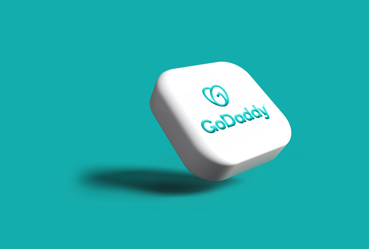 The GoDaddy company logo and wordmark embossed in teal on a floating white cube against a solid teal background